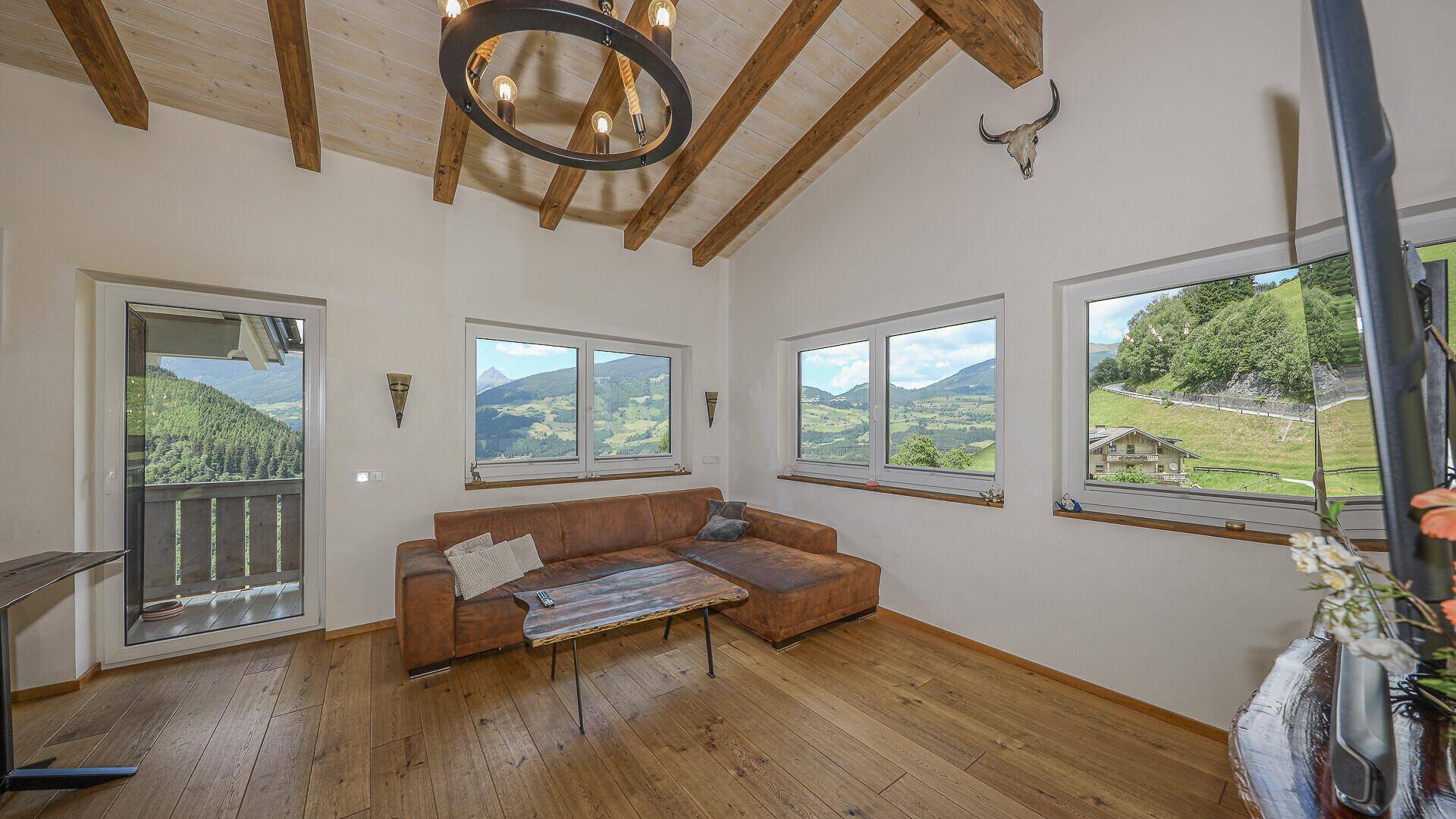 Gemütliches Wohnzimmer mit bequemer Couch, Holzboden und weitem Blick auf die Berge.