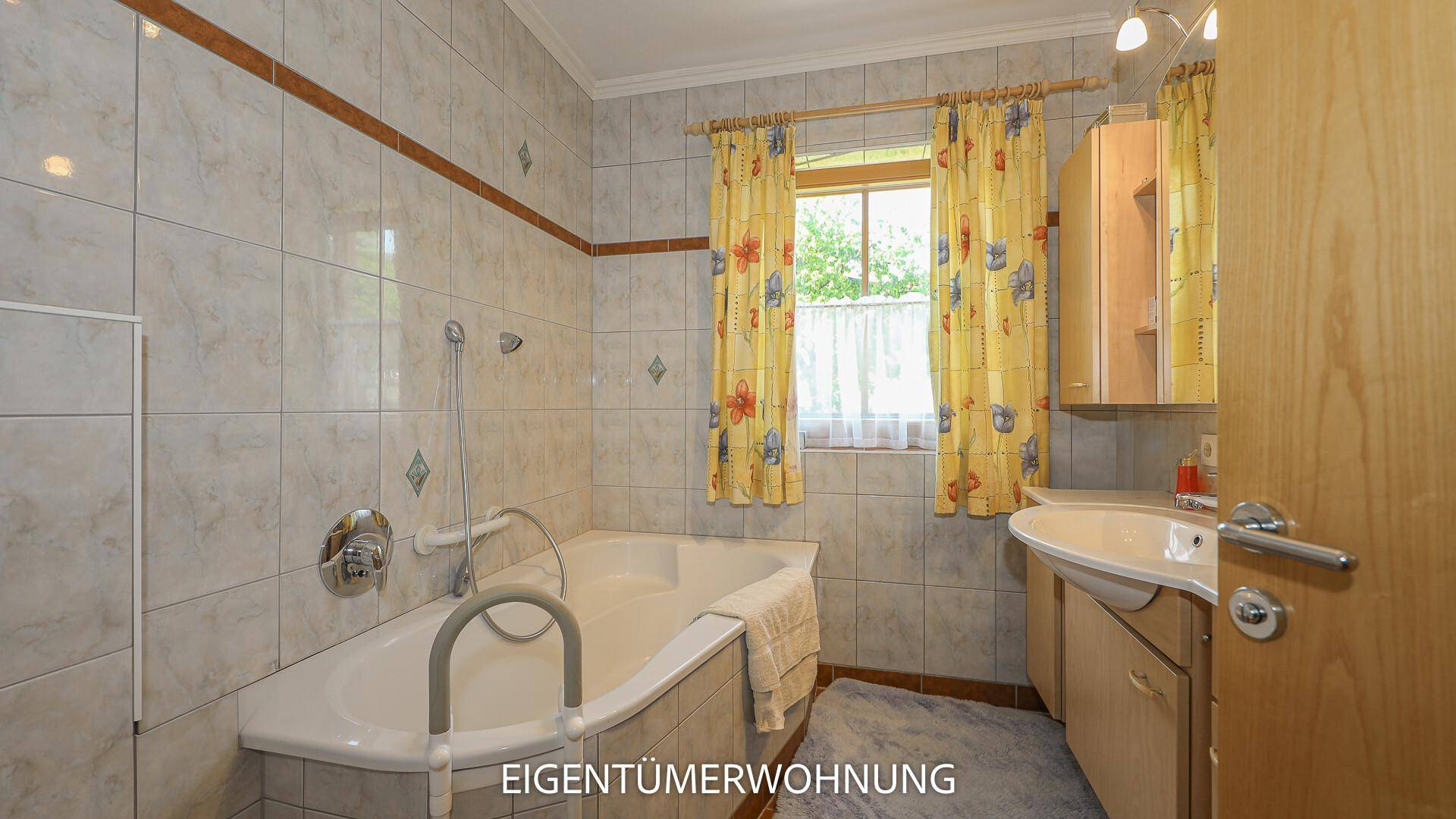 Gefliestes Badezimmer mit Badewanne, Fenster und traditionellen Armaturen.