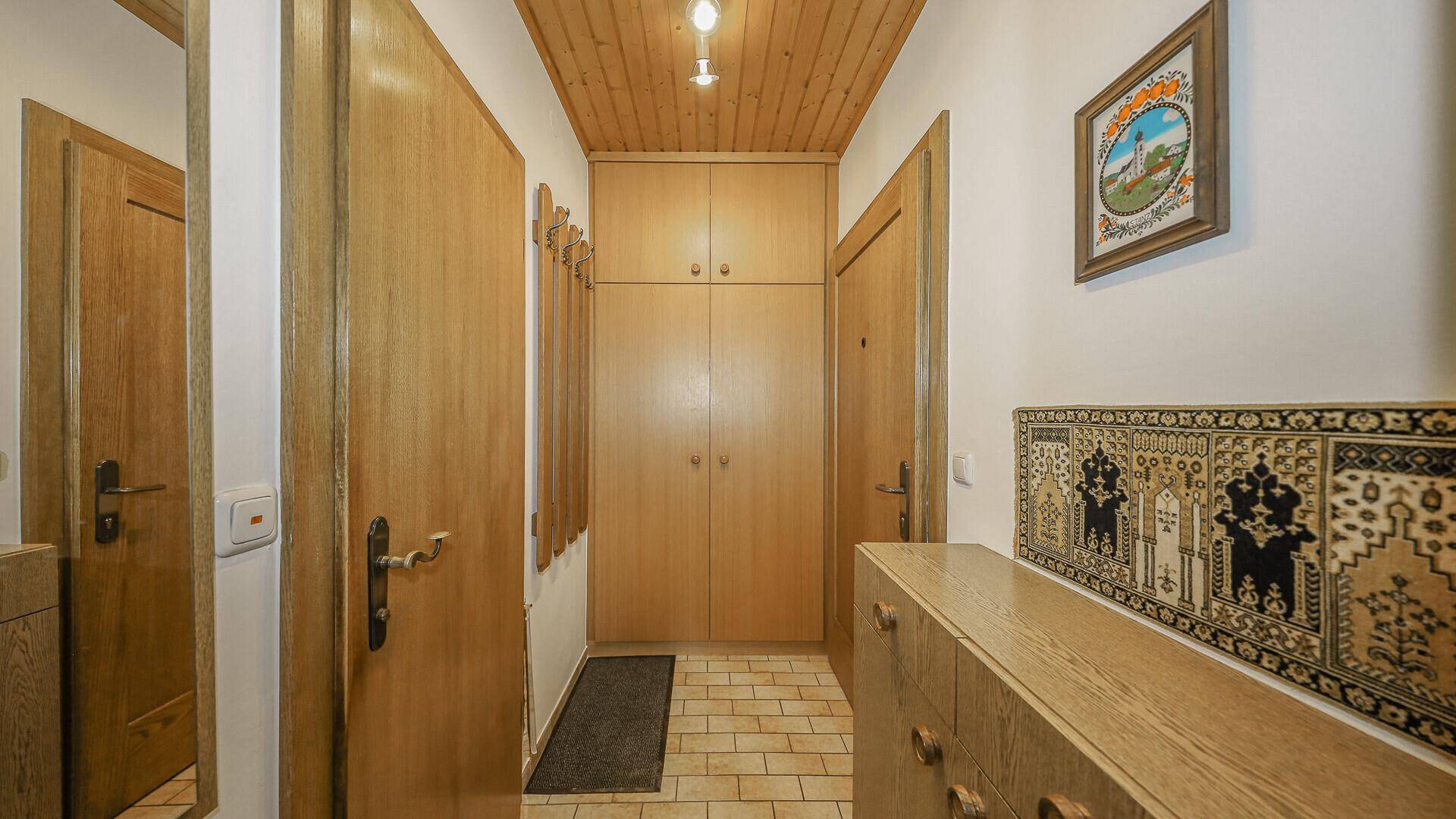 Traditioneller Flur mit Fliesenboden, Holzdecke und praktischen Einbauschränken.
