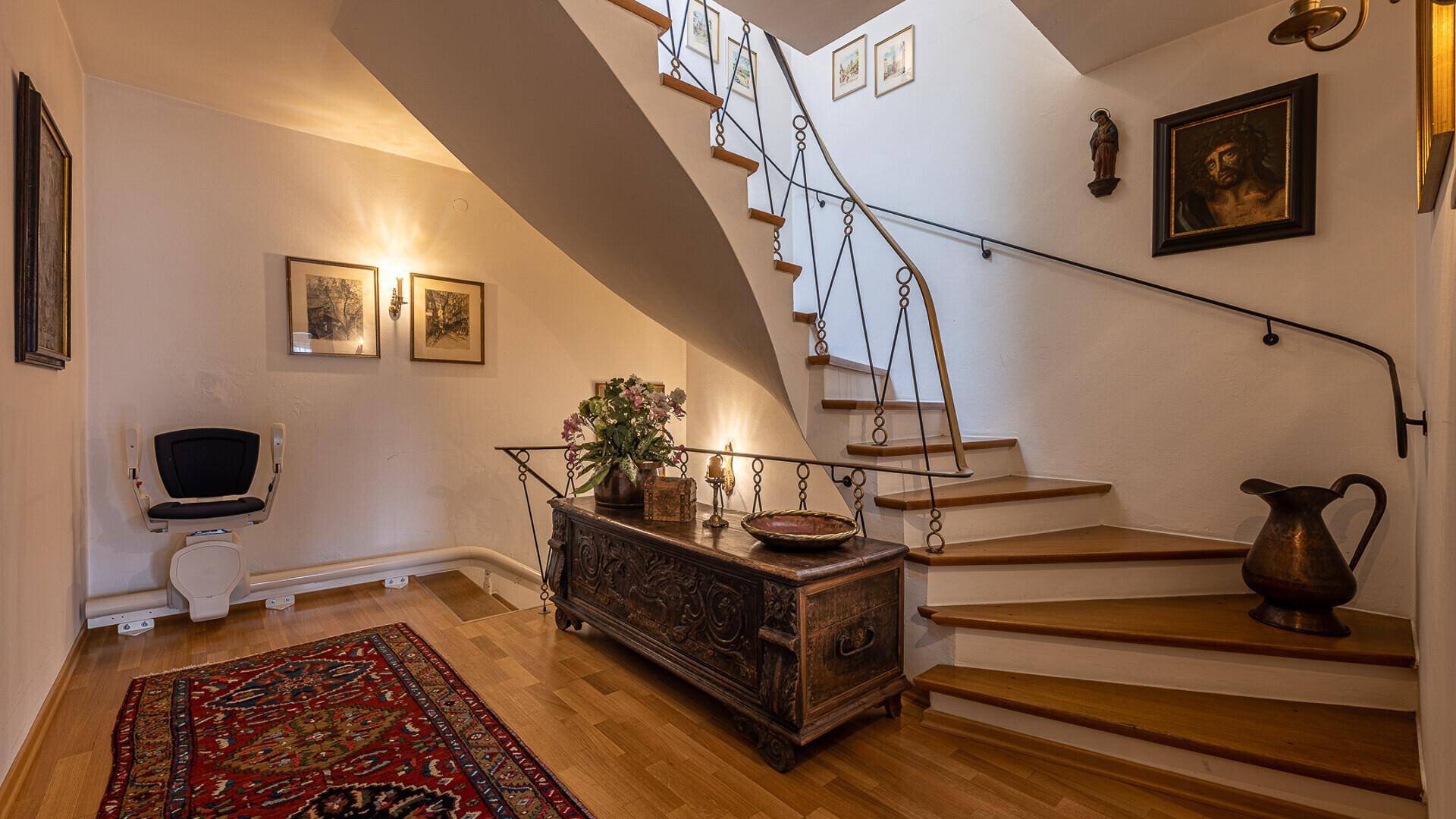 Heller Flur mit Holztreppe, Treppenlift und traditioneller Dekoration.