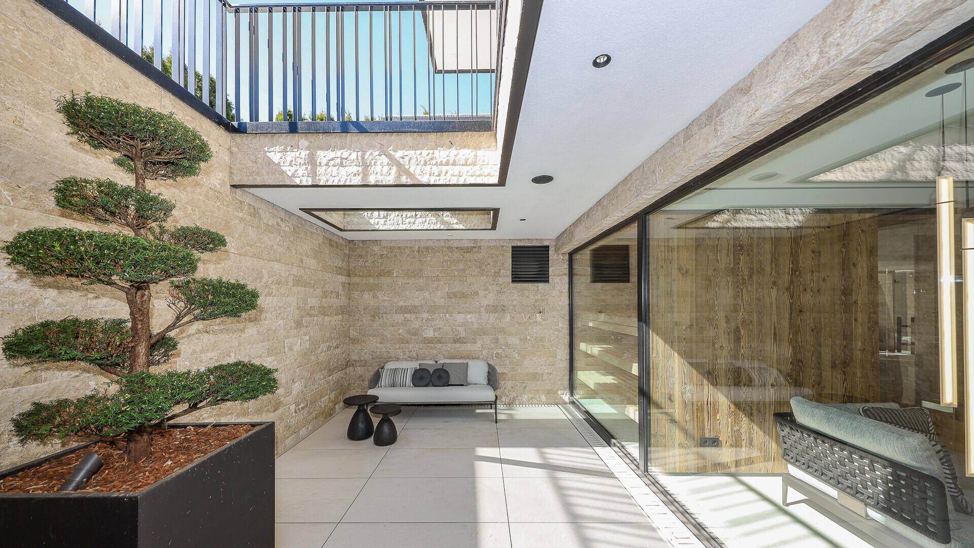 Stilvolle Terrasse mit Zierbaum, Natursteinwand und großen Glasfronten zum Innenbereich.
