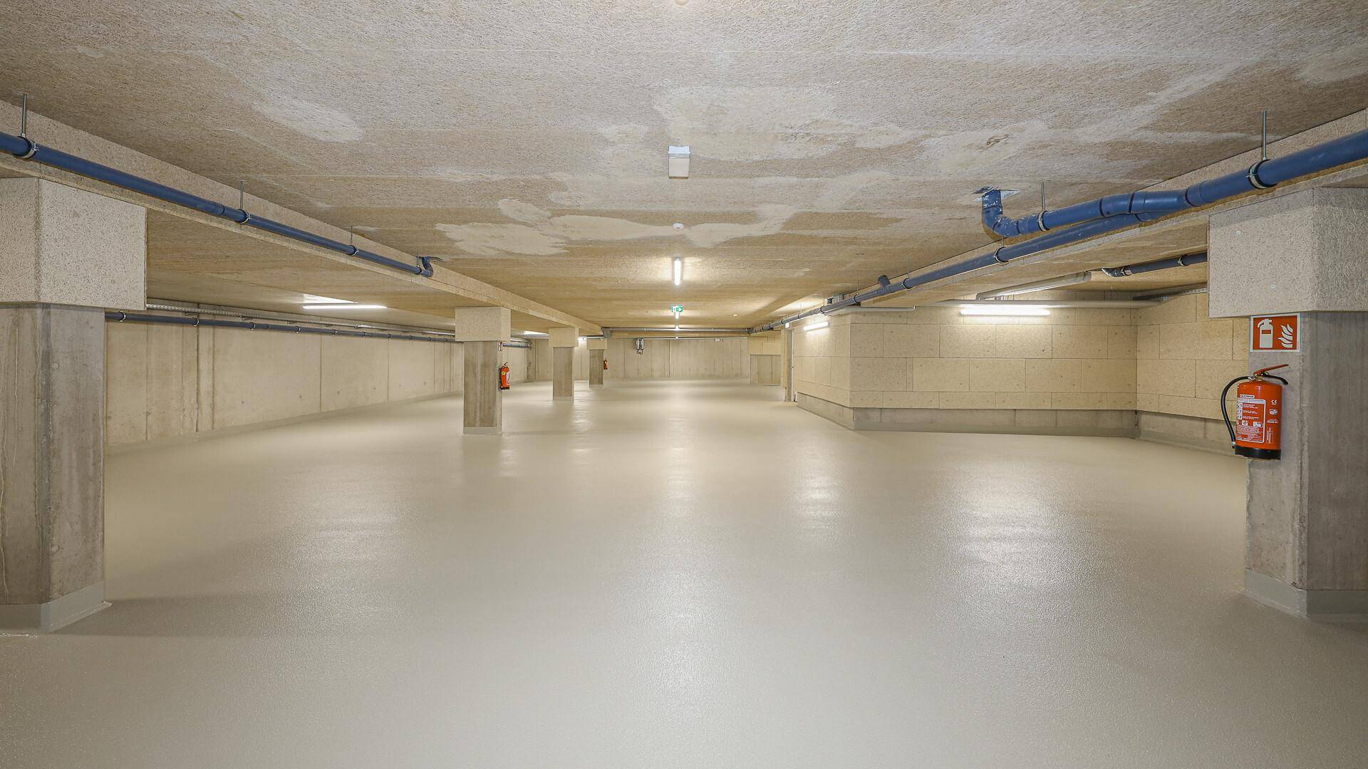 Weitläufige Tiefgarage mit Betonstützen und Brandschutzvorrichtungen, gut beleuchtet.
