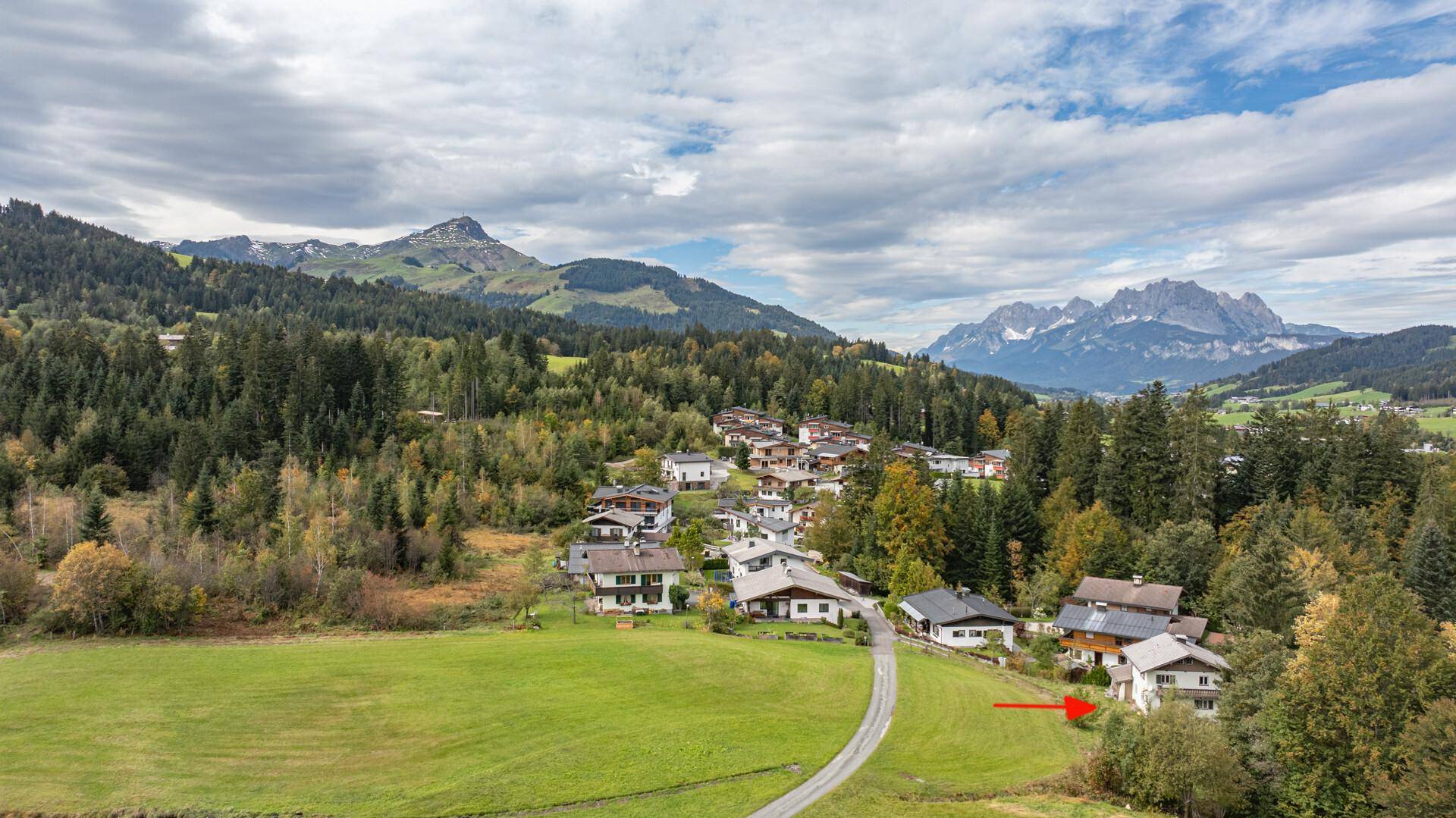 Luftaufnahme einer Wohnsiedlung in den Bergen, mit einem roten Pfeil, der auf ein bestimmtes Haus zeigt.