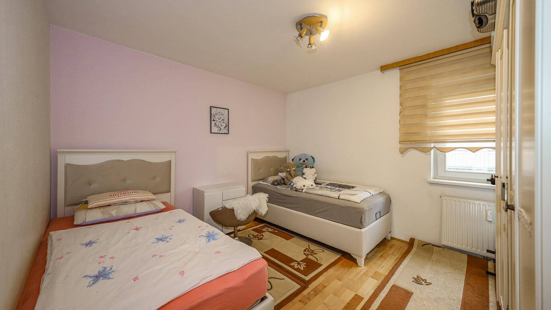 Kinderzimmer mit zwei Einzelbetten, Holzboden und Fenster mit Jalousien.