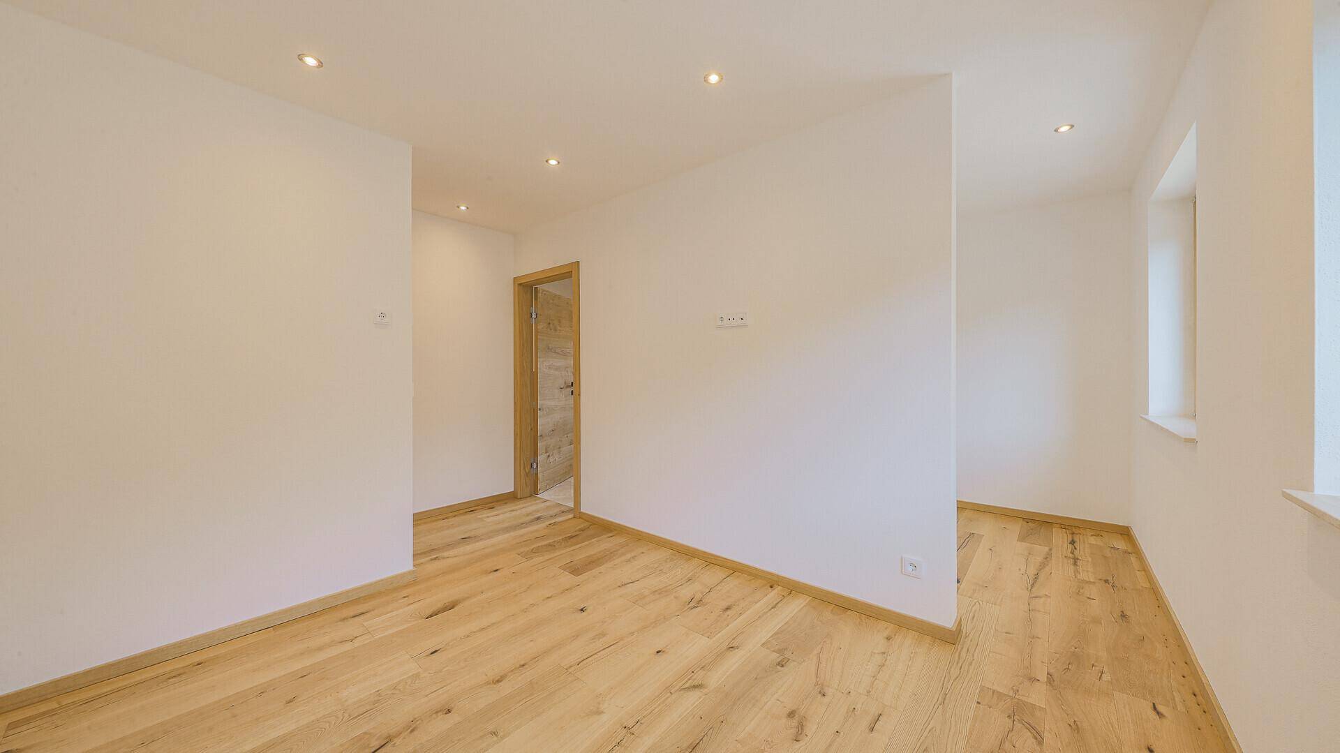 Heller, leerer Flur mit Holzboden und weiß gestrichenen Wänden.