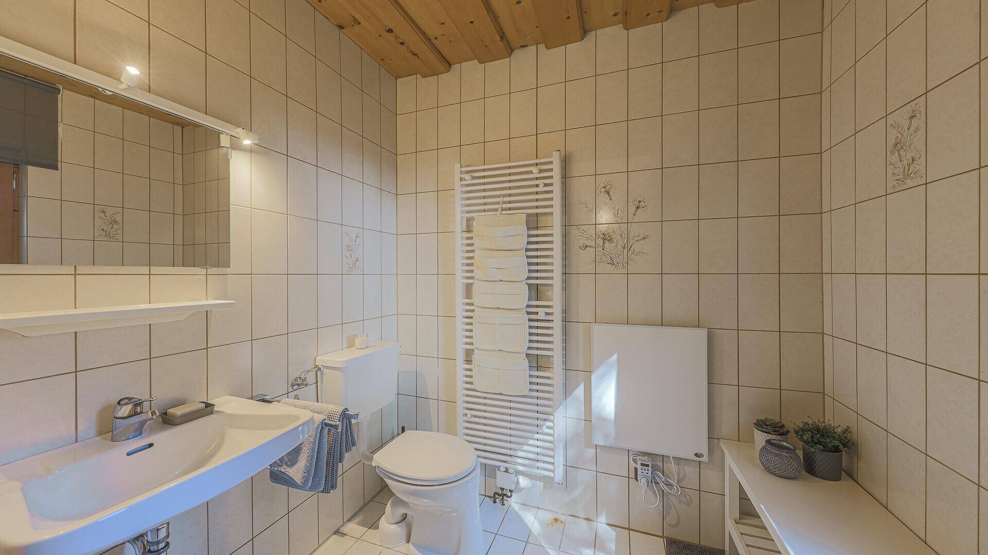 Helles Badezimmer mit Fliesen, Waschtisch, Toilette und beheiztem Handtuchhalter.
