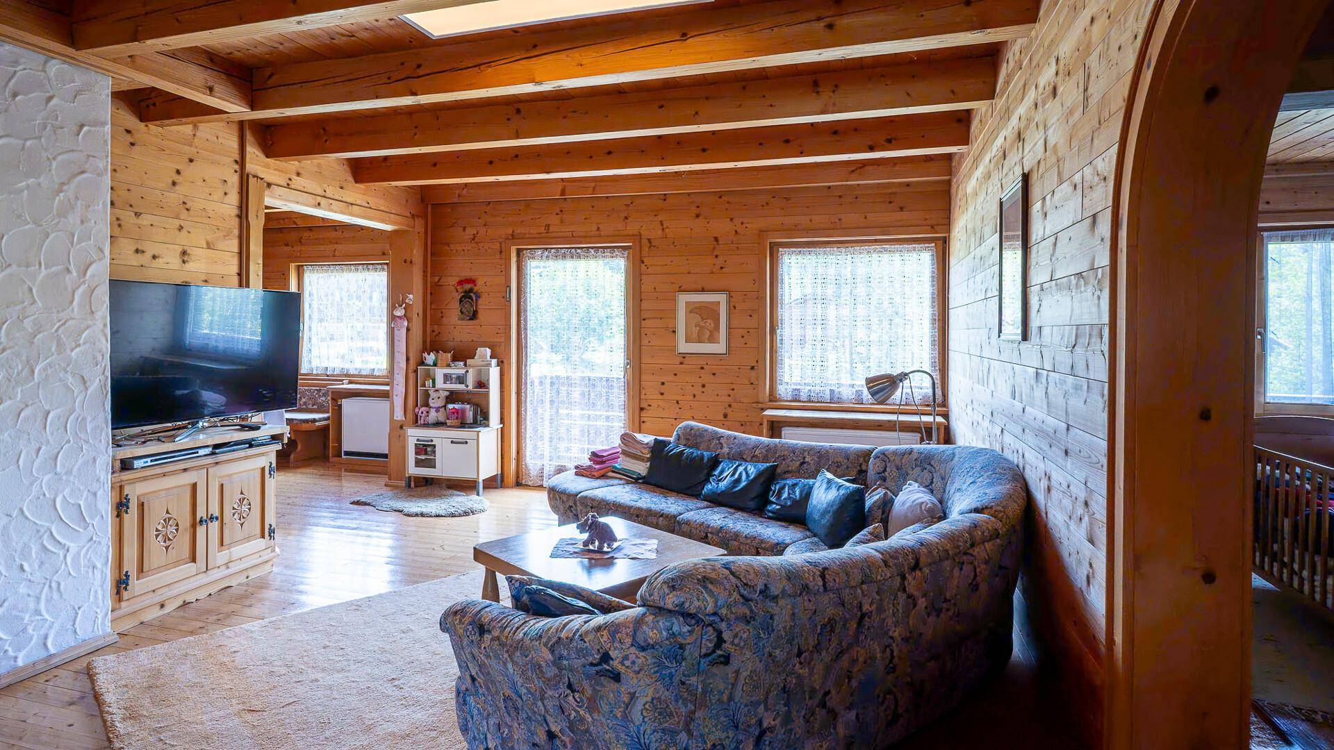 Gemütliches Wohnzimmer im alpinen Stil mit Holzvertäfelung, bequemer Couch und Balkonzugang.