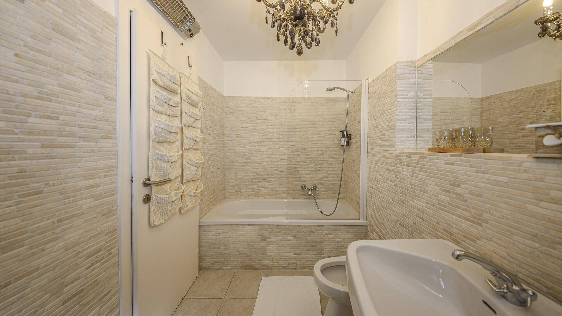 Modernes Badezimmer mit Badewanne, Dusche und beigefarbenen Fliesen an den Wänden.