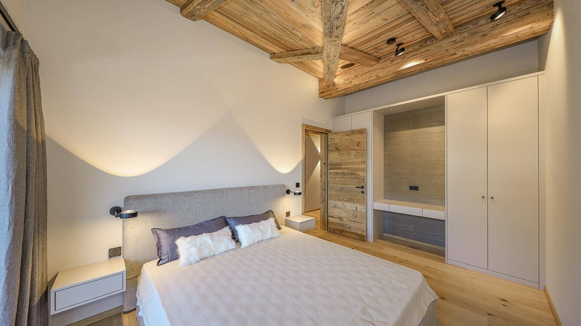 Modernes Schlafzimmer mit Holzbalkendecke, Einbauschränken und integriertem Schminktisch.