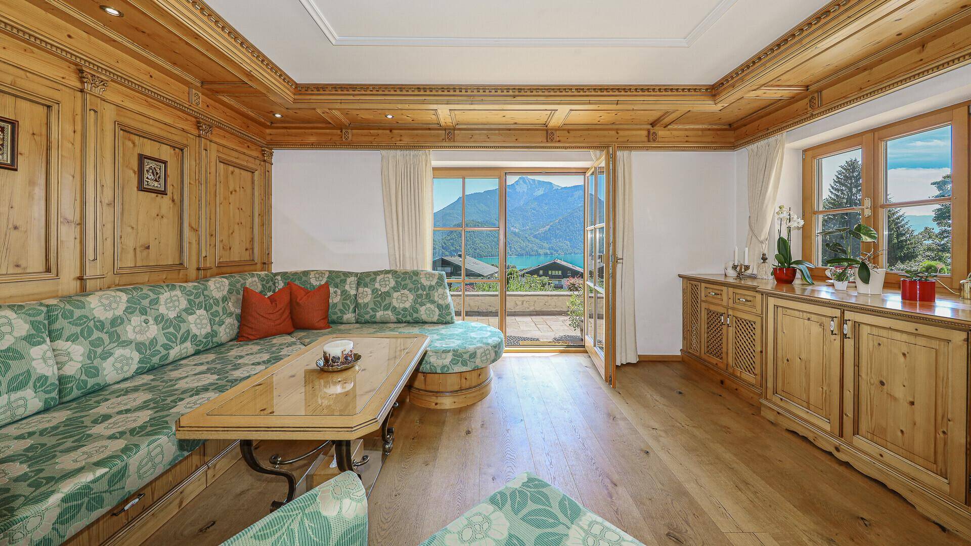 Heller Wohnbereich mit Holztäfelung, Zugang zur Terrasse und beeindruckendem Berg- und Seeblick.