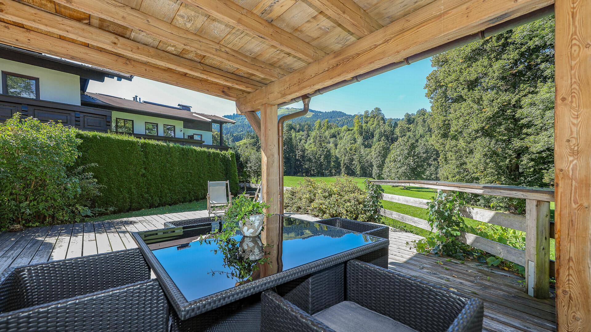 Überdachte Holzterrasse mit Lounge-Möbeln und Panoramablick auf die Berge.