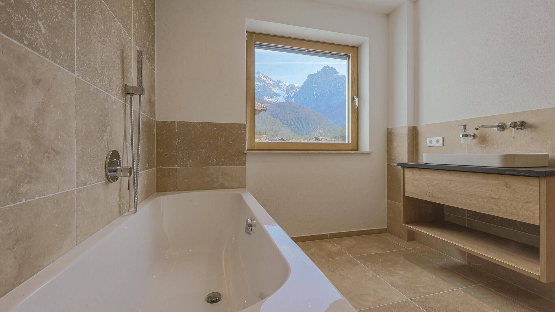 Helles Badezimmer mit Badewanne, Einzelwaschbecken und Fenster mit beeindruckendem Bergblick.