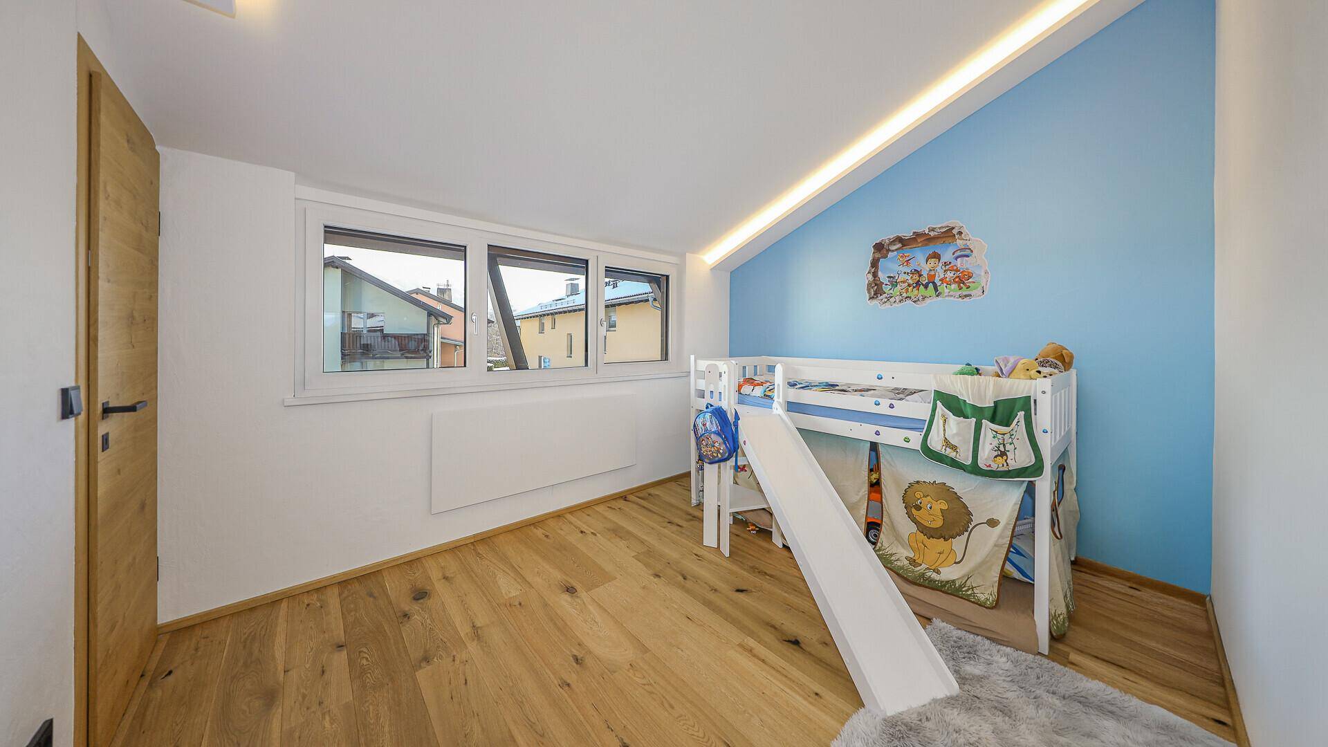 Kinderzimmer mit Holzboden, blau akzentuierter Wand und Hochbett mit Rutsche.