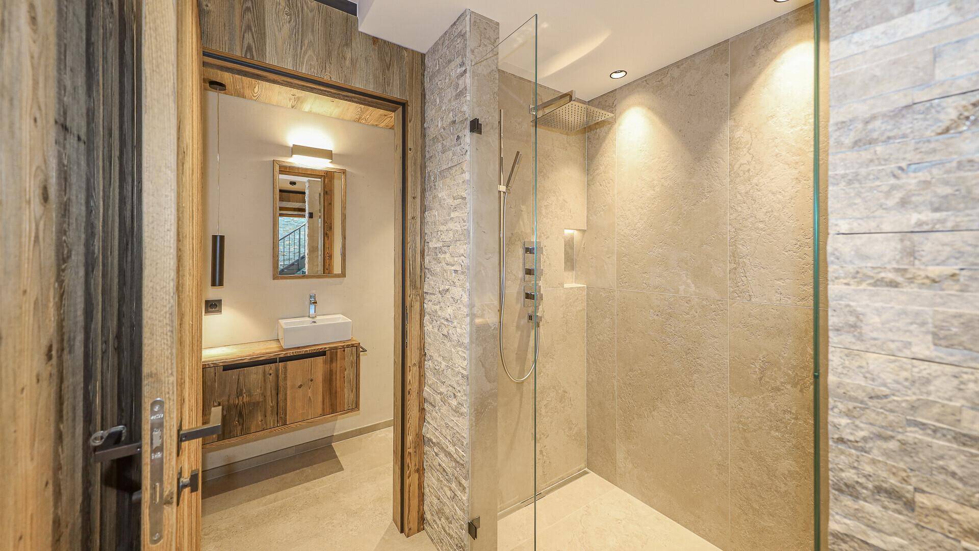 Modernes Badezimmer mit begehbarer Dusche und Steinwand, verbunden mit einem weiteren Bad.