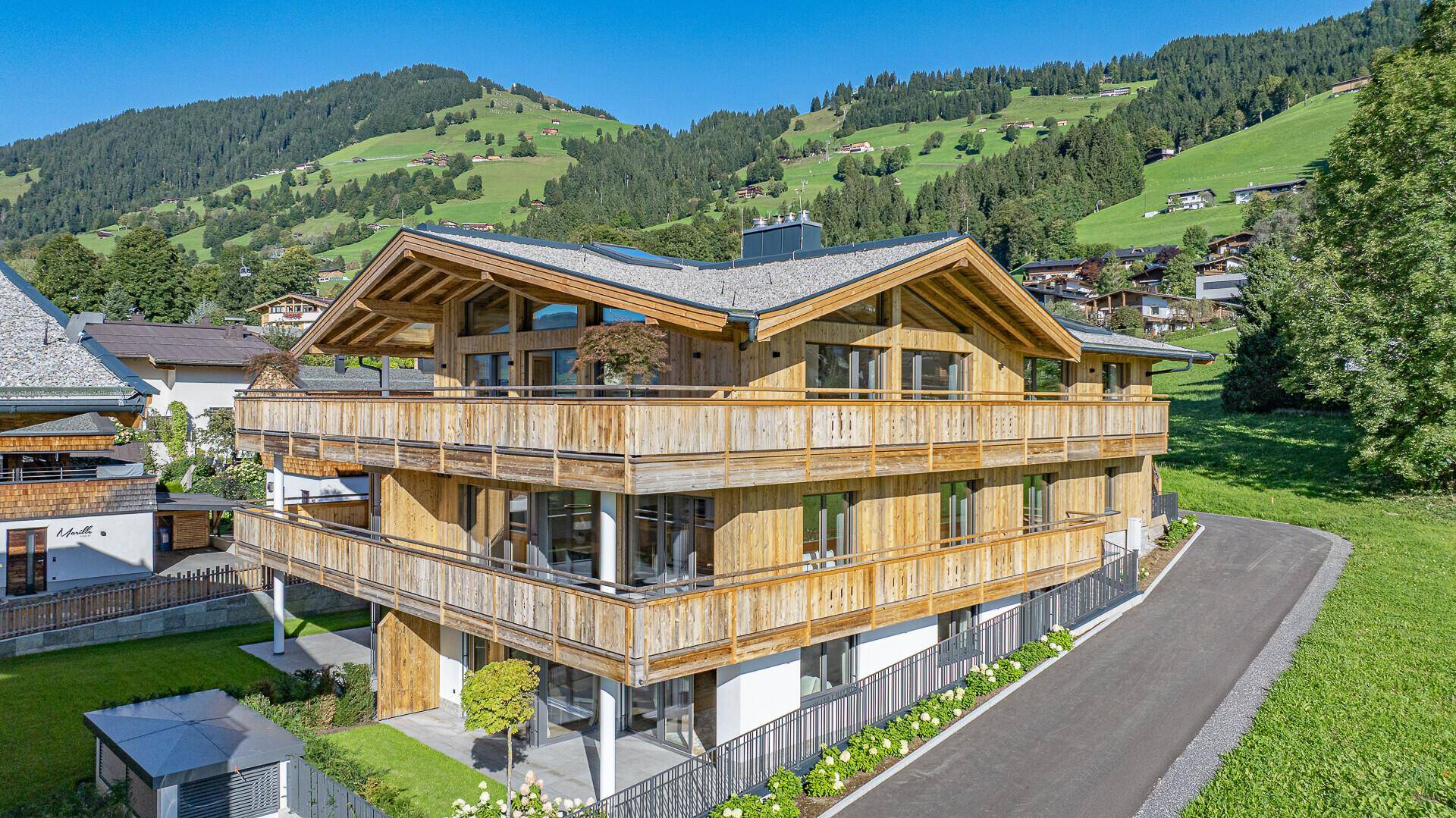 Attraktives Mehrfamilienhaus im alpinen Stil mit Holzbalkonen und Bergblick, bei Tageslicht.