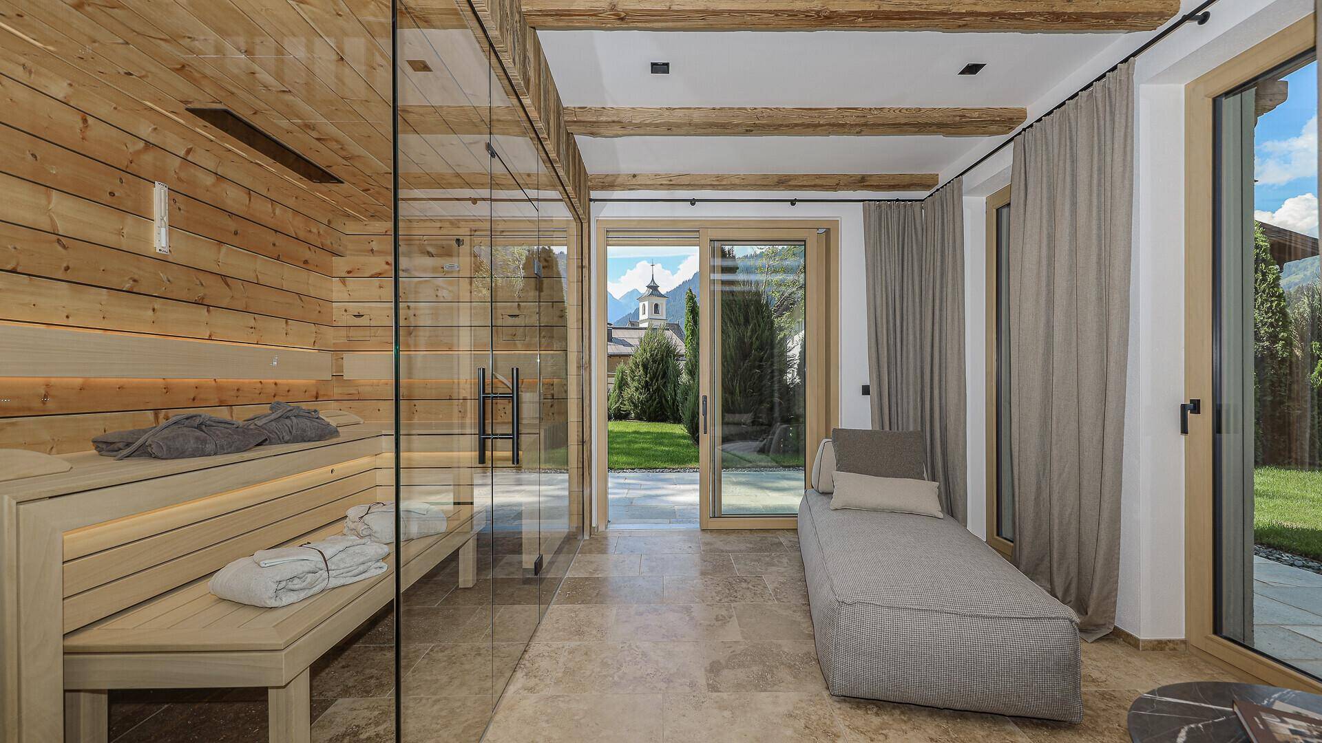 Helle Sauna mit Glasfront und Entspannungsbereich, mit Blick auf den Garten und die Berge.