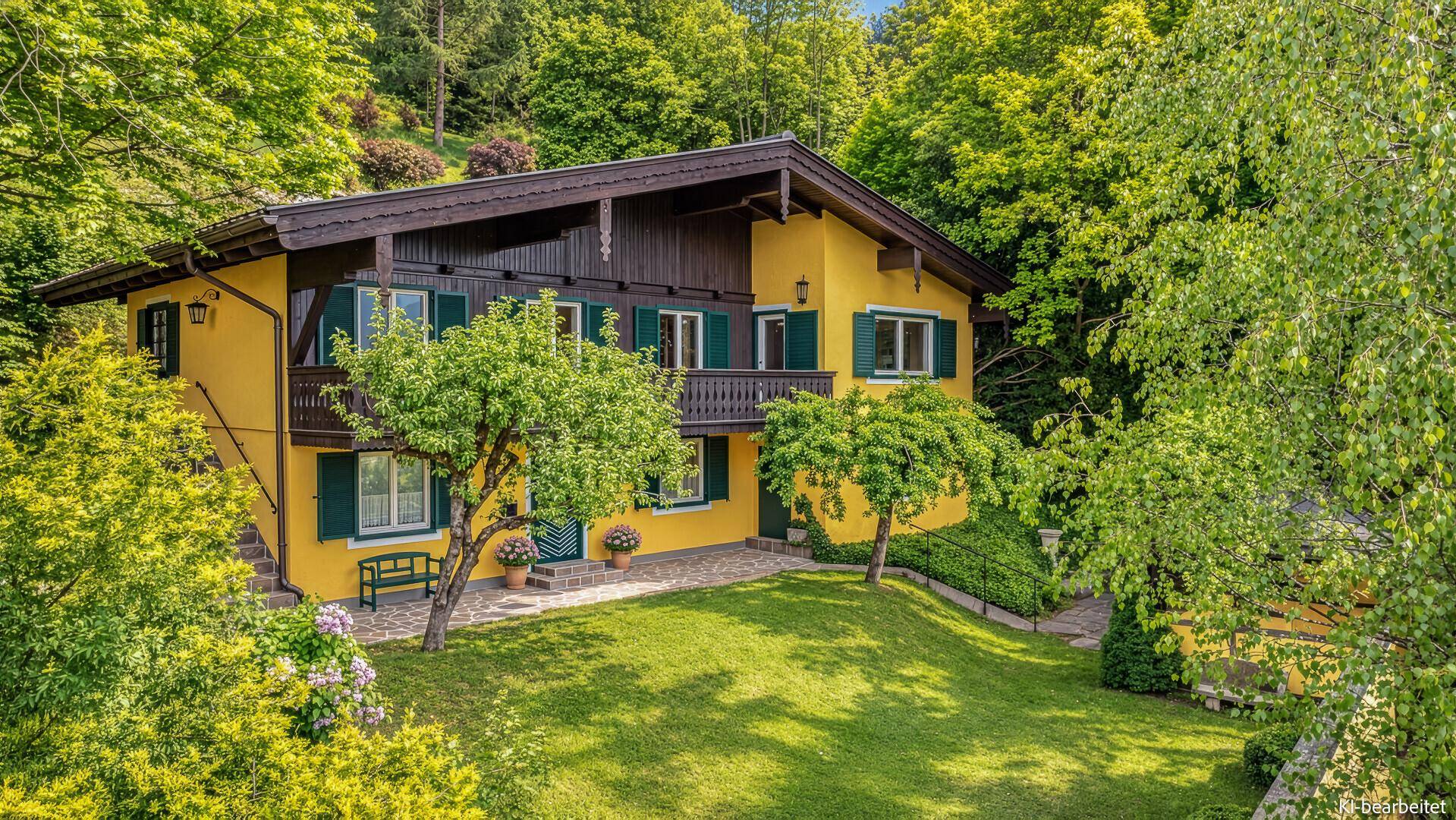 Gelbes Haus mit grünen Fensterläden und braunem Dach, umgeben von einem gepflegten Rasen und Bäumen.