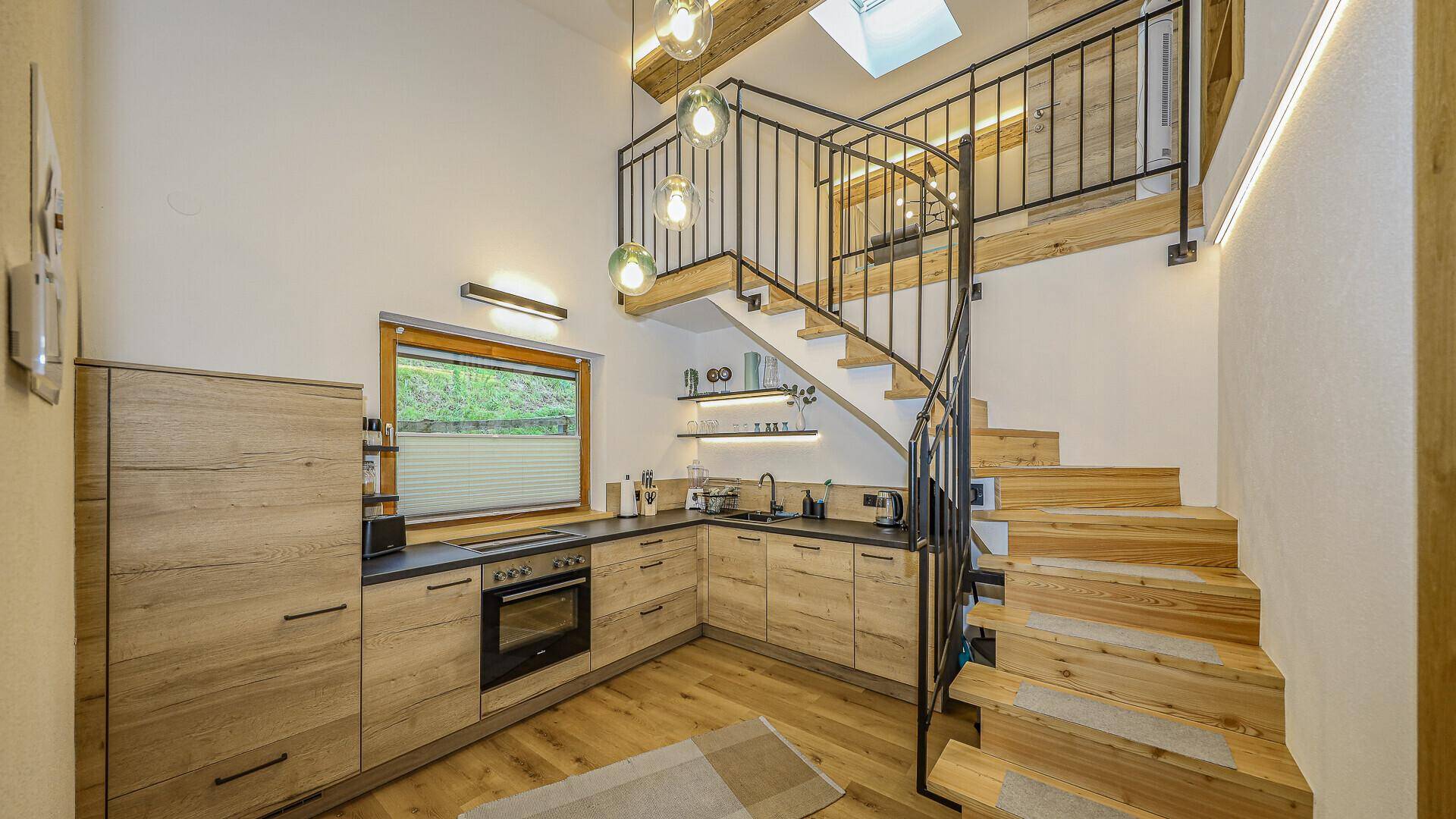 Moderne Küche mit Holzfronten, schwarzer Arbeitsplatte und einer eleganten Wendeltreppe zu einer Galerie.