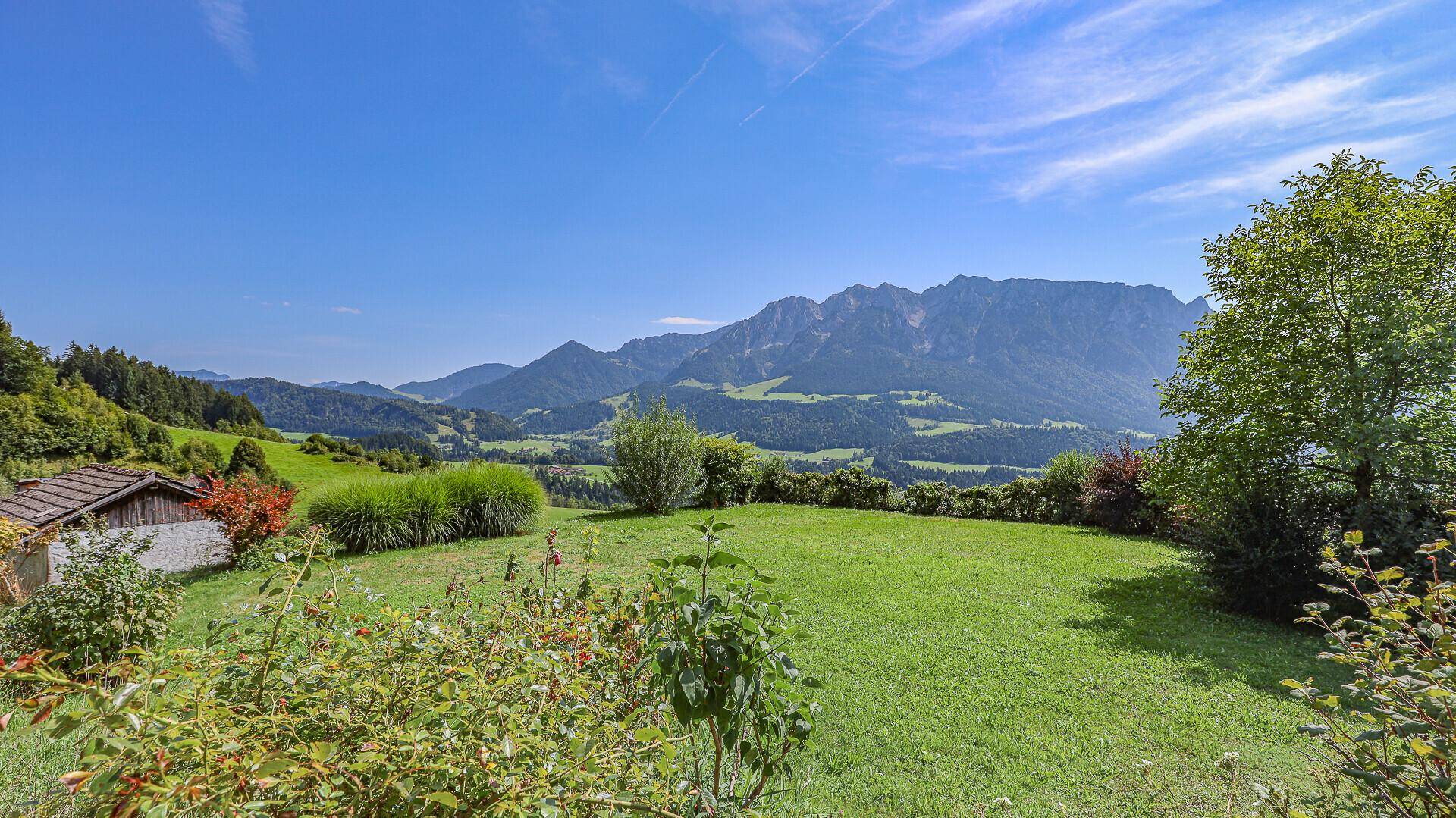 Weitläufiger Gartenbereich mit Panoramablick auf die umliegende Berglandschaft unter blauem Himmel.