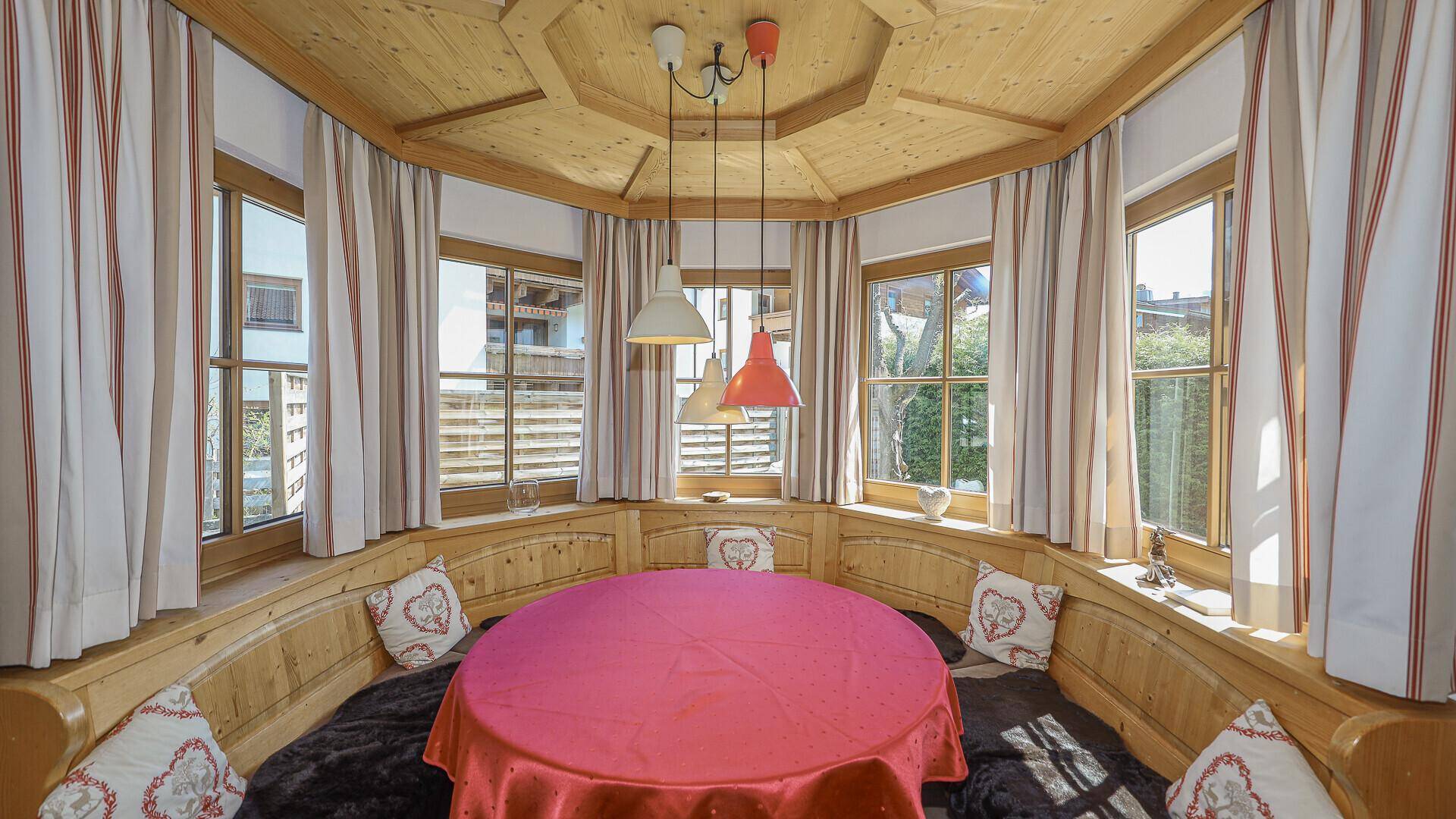 Traditioneller Essbereich mit runder Eckbank, vielen Fenstern und Holzbalkendecke.