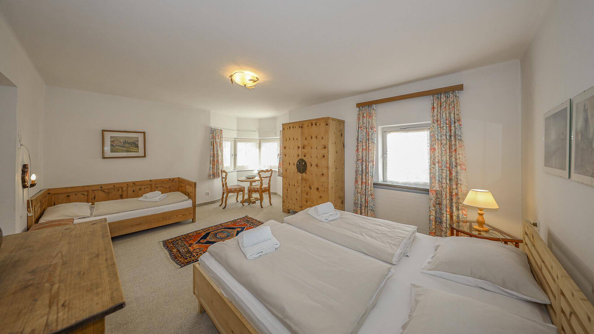 Geräumiges Schlafzimmer mit Doppelbett, Einzelbett, Holzschrank und einem kleinen Esstisch.