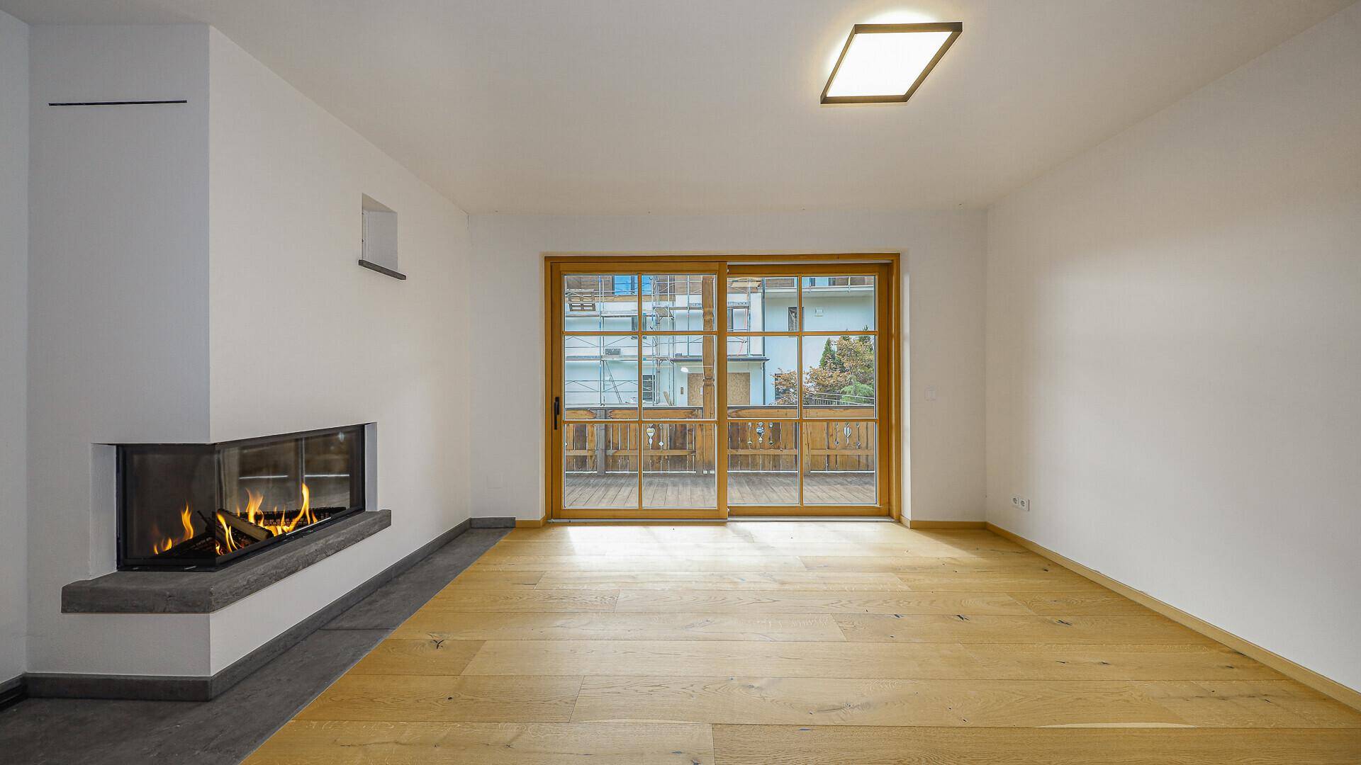 Heller Wohnbereich mit Holzboden, Eckkamin und Zugang zu einem Balkon.