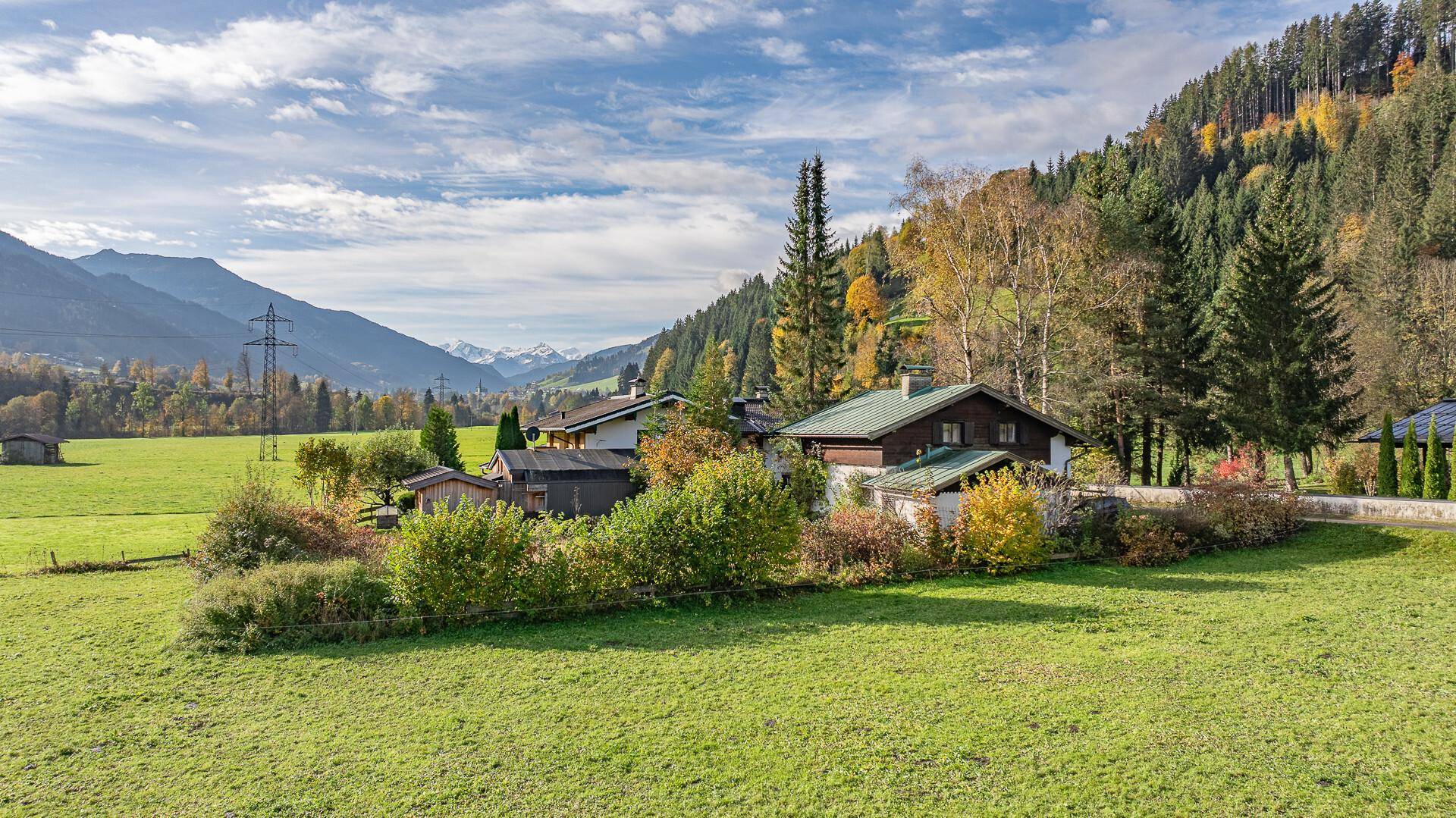 Ländliche Umgebung mit traditionellen Häusern, grünen Wiesen und bewaldeten Hügeln unter blauem Himmel.