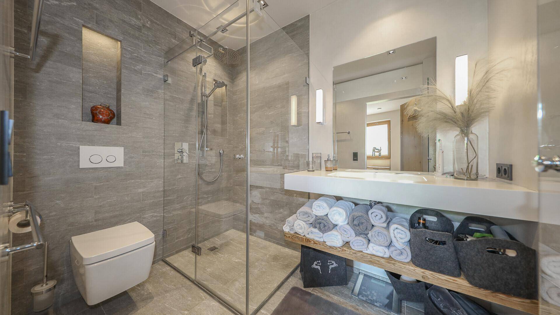 Elegantes Badezimmer mit bodengleicher Dusche, Wand-WC und großem Spiegel.
