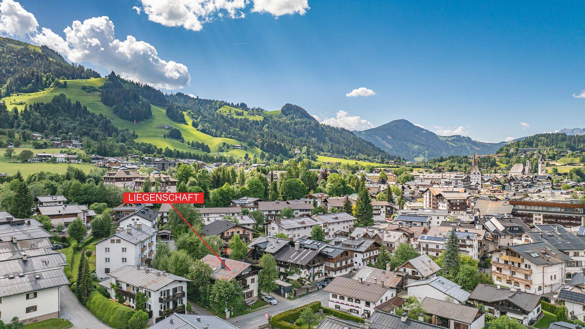 Luftaufnahme einer Bergstadt mit markierter Liegenschaft und umliegender Naturlandschaft.