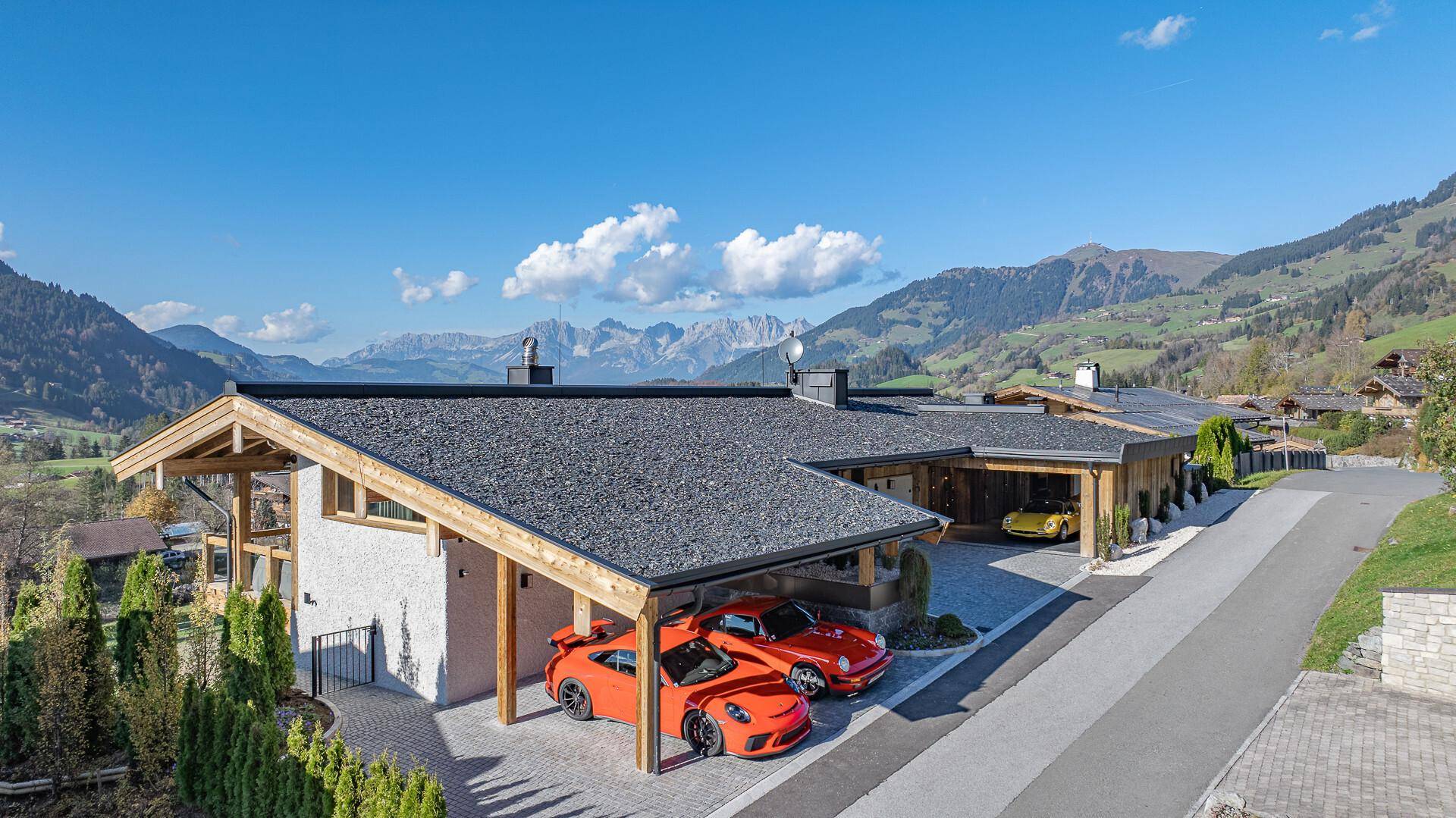 Modernes Chalet mit Carport und beeindruckendem Bergblick, umgeben von grüner Natur.