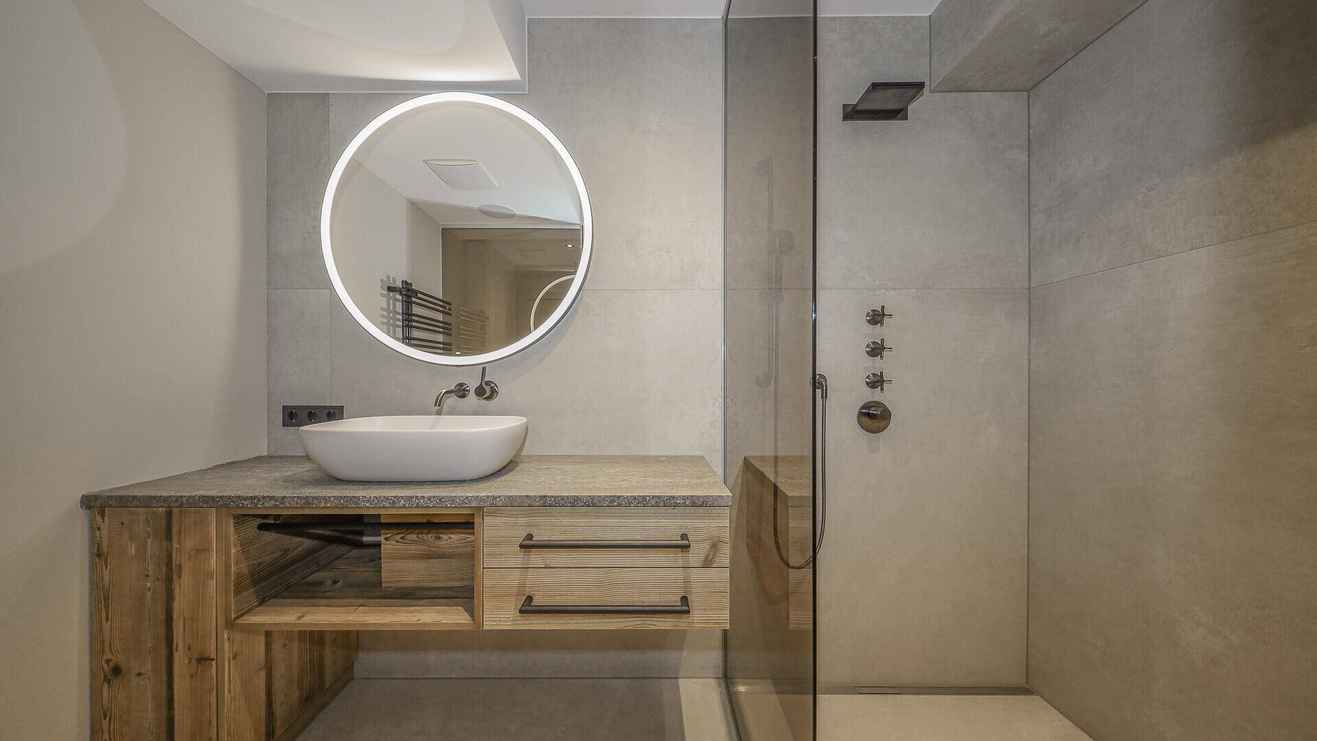 Modernes Badezimmer mit rundem Spiegel, Waschtisch und begehbarer Dusche.