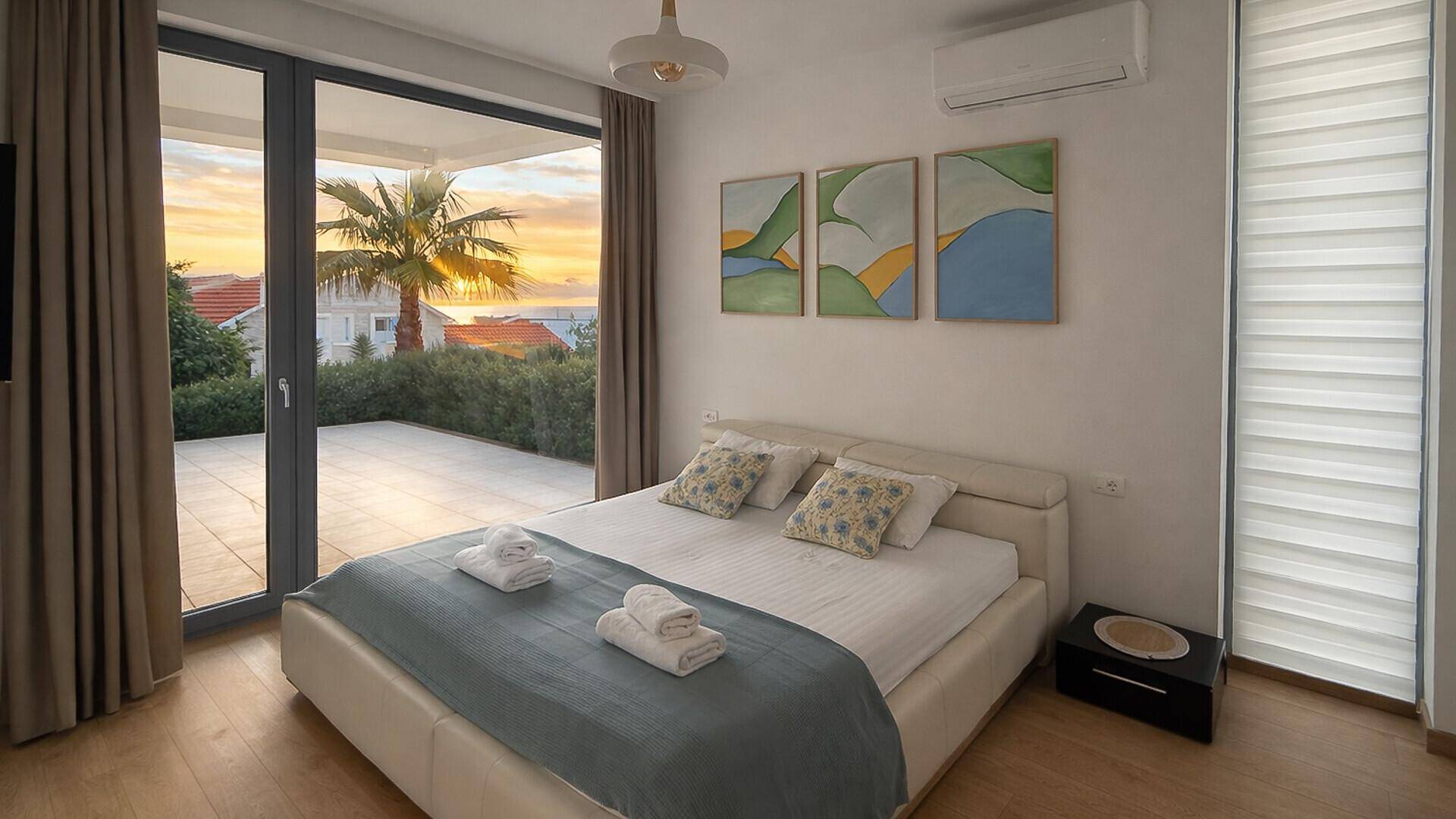Helles Schlafzimmer mit Doppelbett, Holzboden und direktem Zugang zur Terrasse mit Meerblick.
