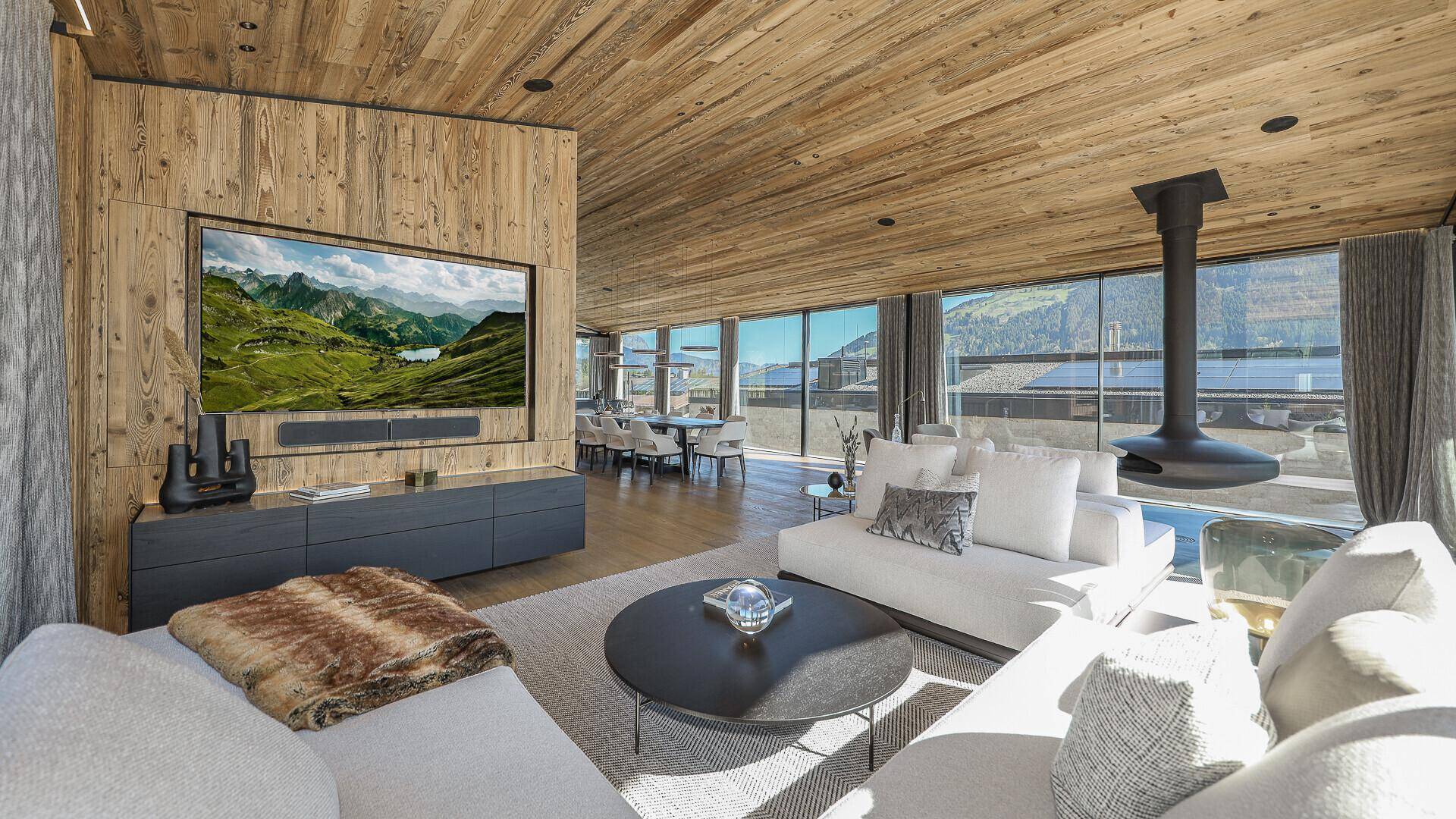 Gemütlicher Wohnbereich mit Holzwänden, großem Fernseher und freistehendem Kamin, umgeben von Natur.
