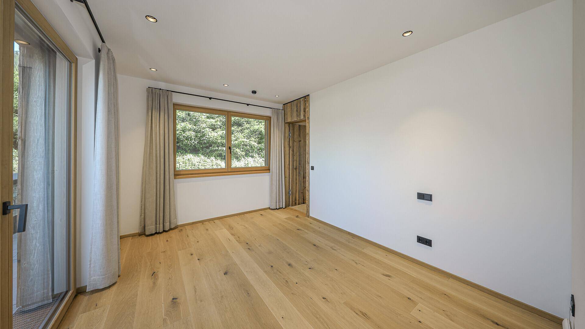 Helles Zimmer mit Holzboden und Fenster mit Blick ins Grüne.