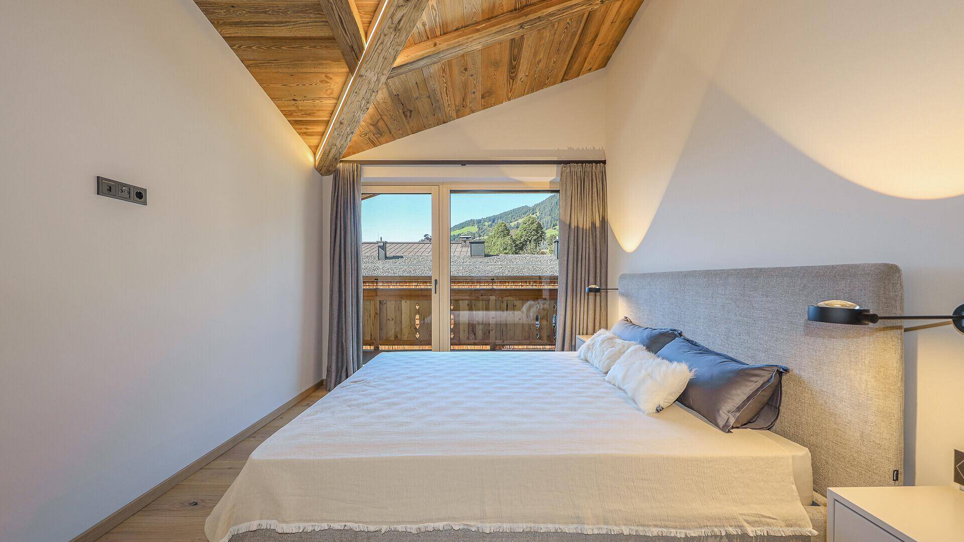 Helles Schlafzimmer mit Holzbalkendecke und Fenster mit Blick auf die umliegende Landschaft.