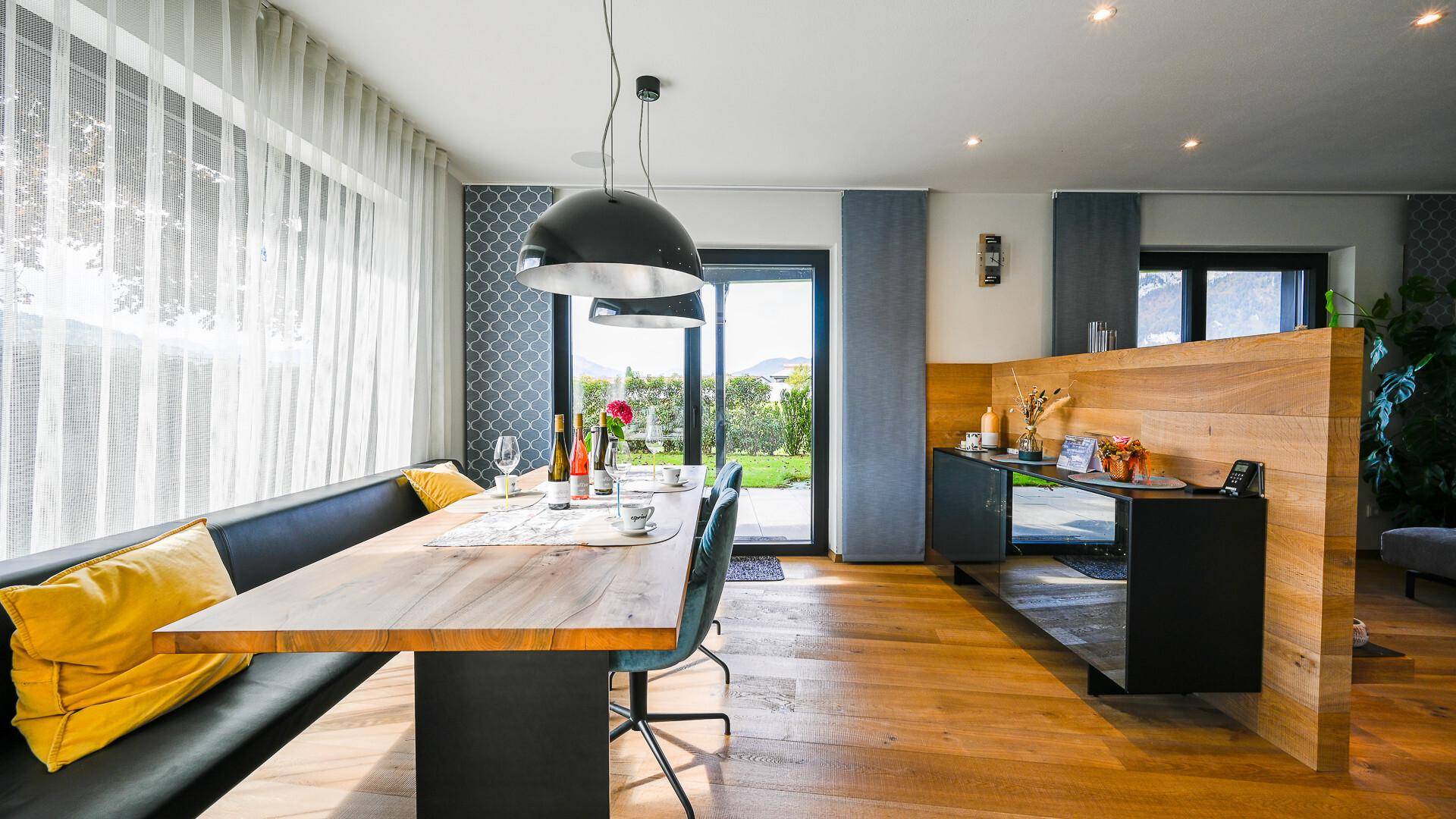 Gemütlicher Essbereich mit Holztisch, Sitzbank und großen Fenstern mit Blick ins Grüne.