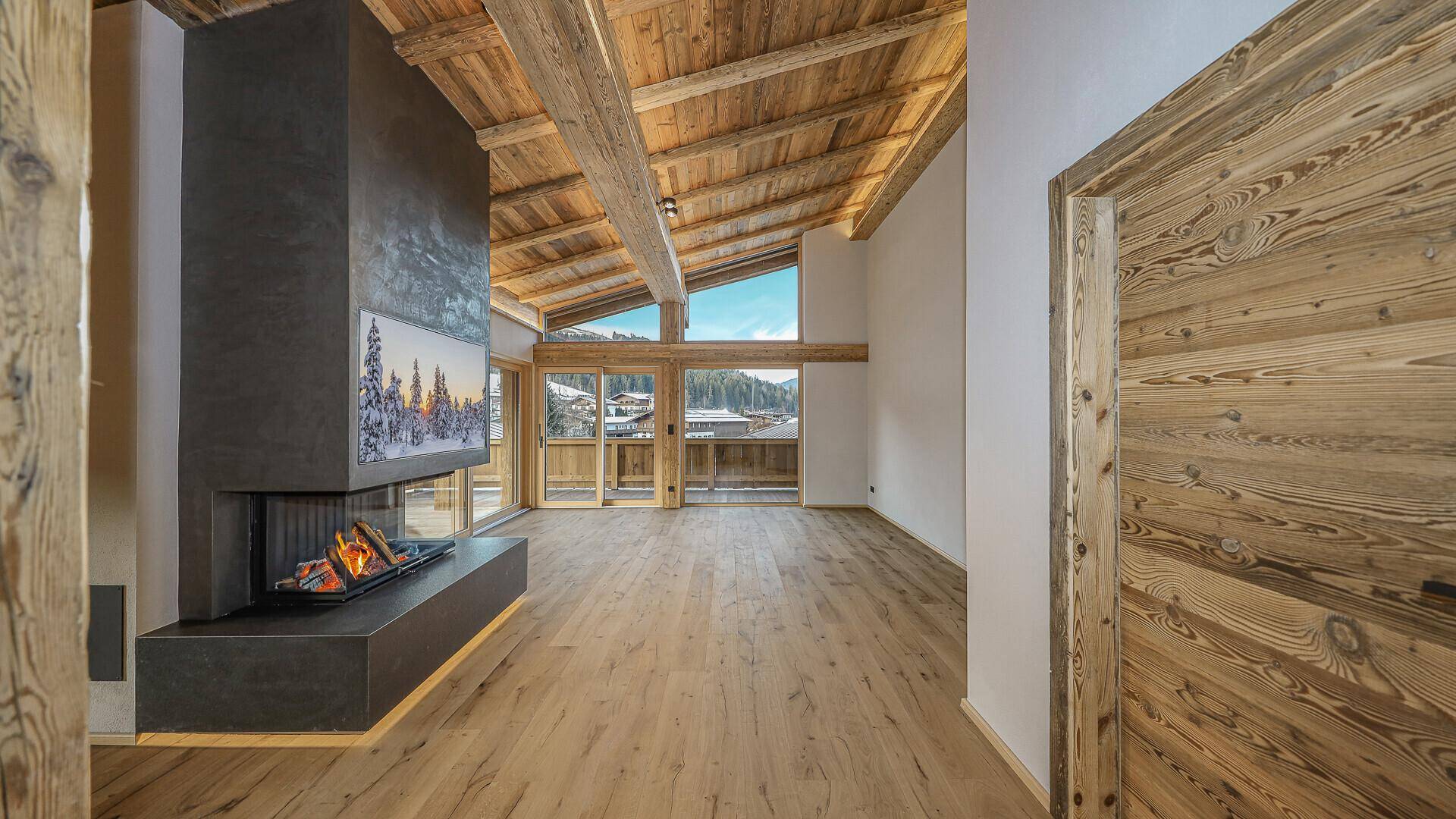 Großzügiges Wohnzimmer mit modernem Kamin, Holzbalkendecke und Zugang zu einem Balkon.