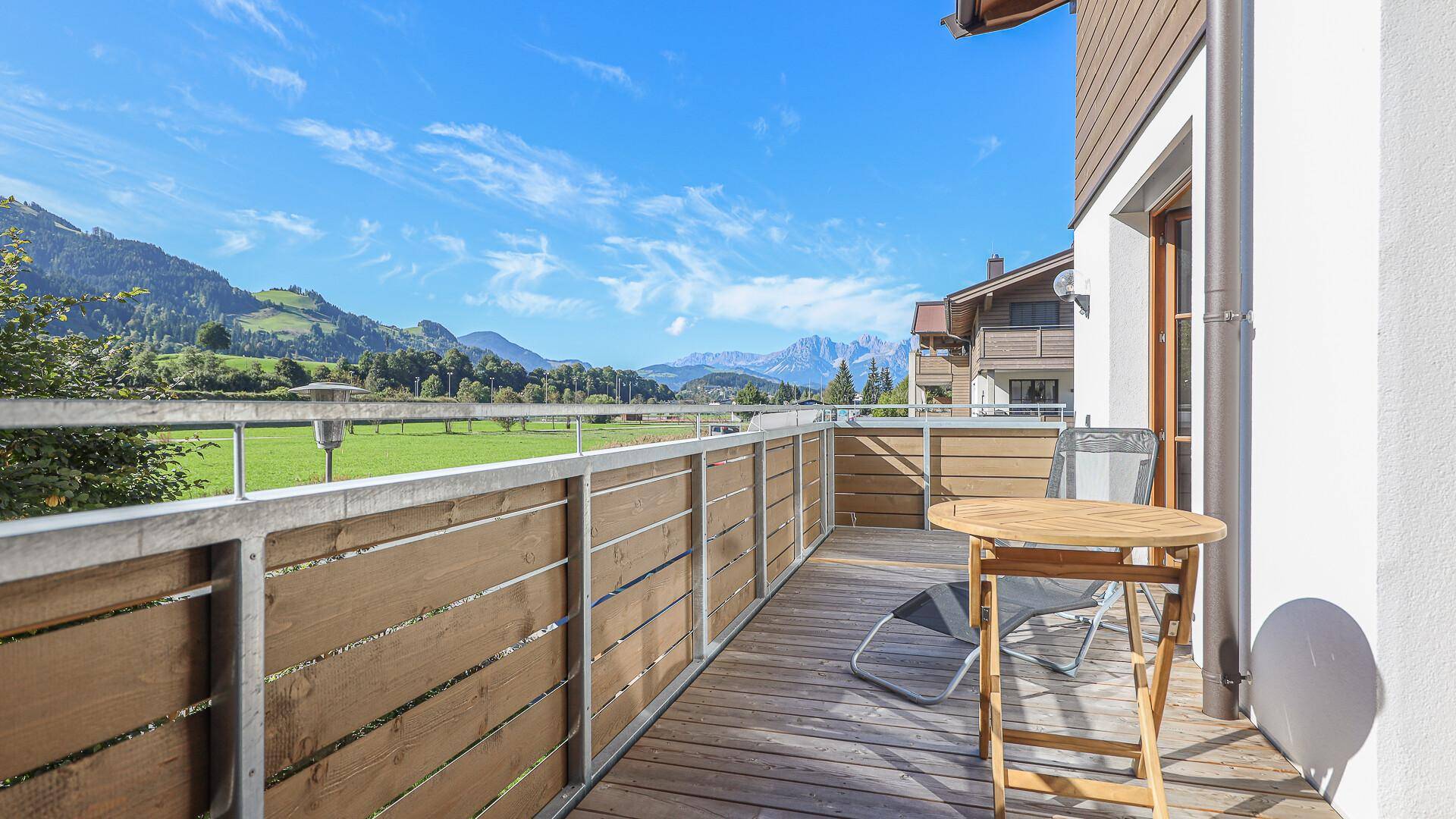 Geräumiger Balkon mit Holzboden, Sitzgelegenheiten und weitem Blick auf die Berge.