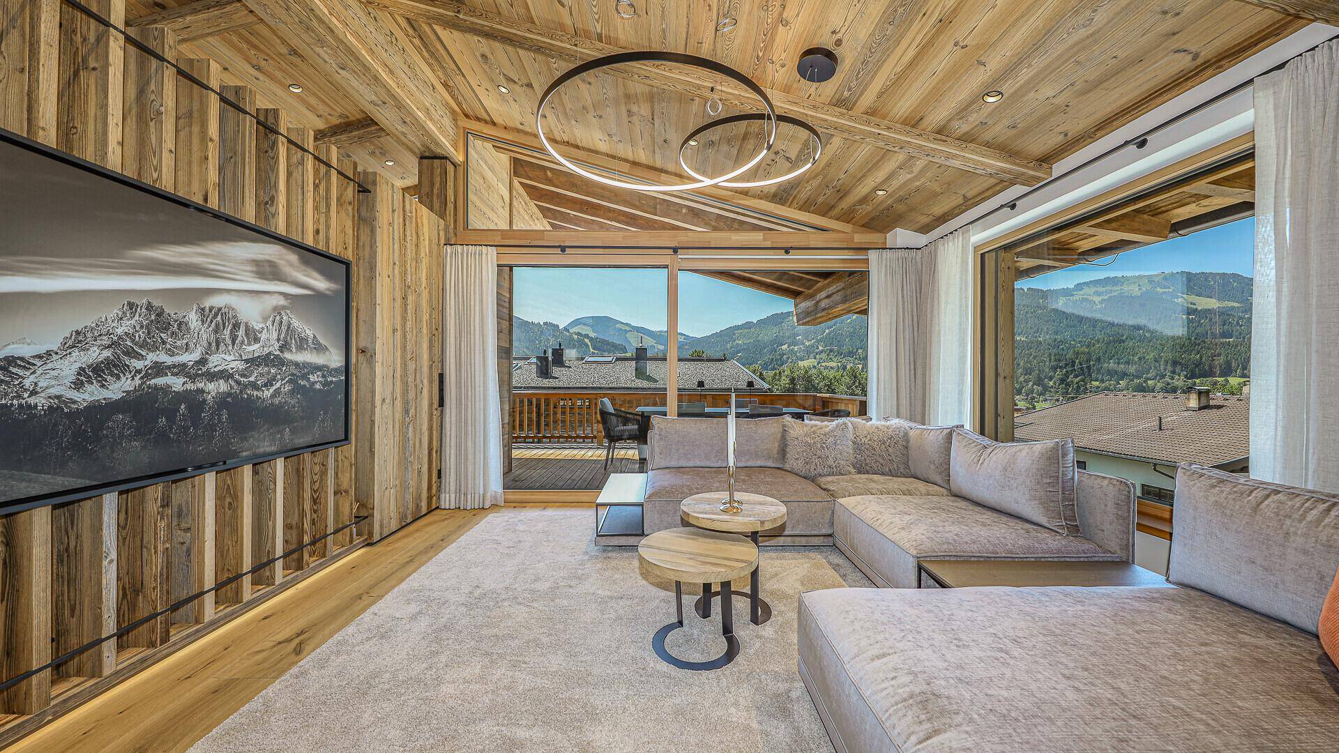 Gemütliches Wohnzimmer mit Ecksofa, Holzwänden und großem Fenster mit Bergblick.