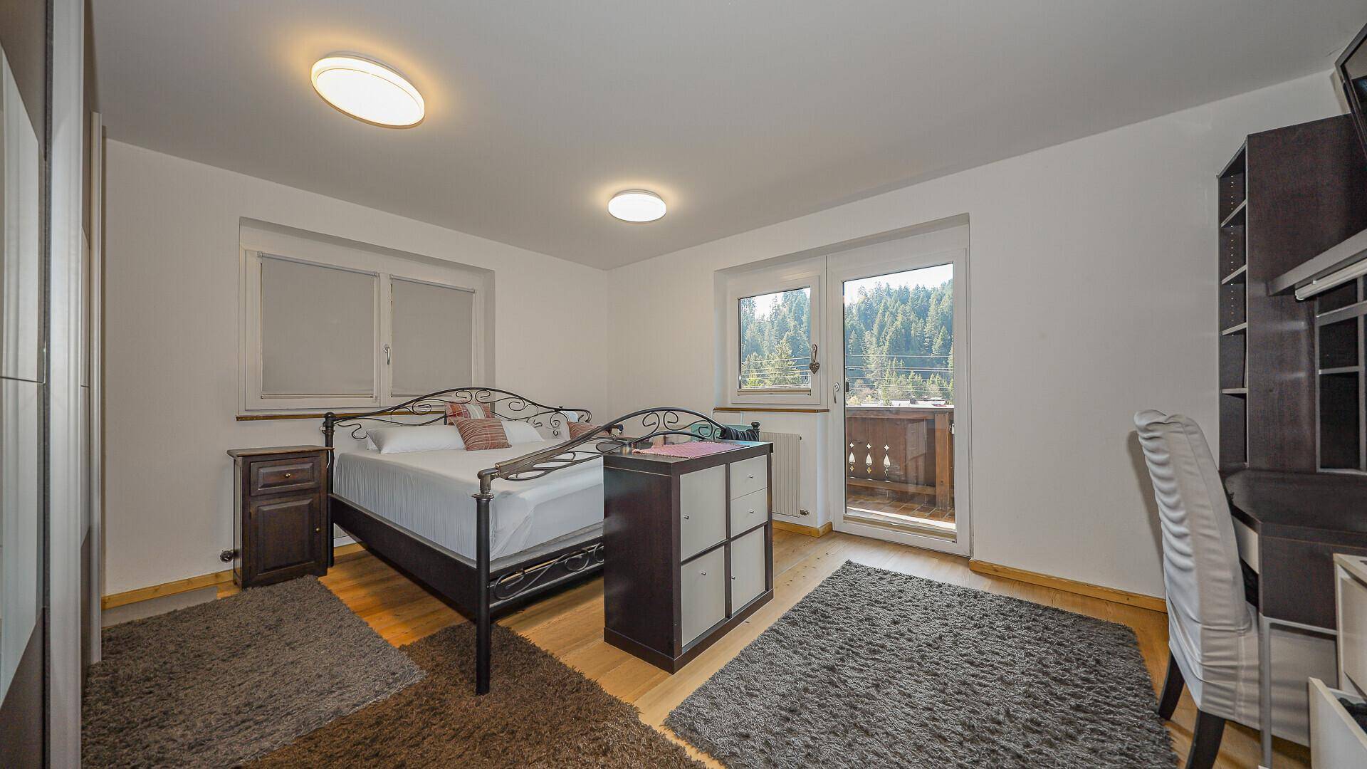 Helles Schlafzimmer mit Balkonzugang und Blick auf die bewaldete Umgebung.