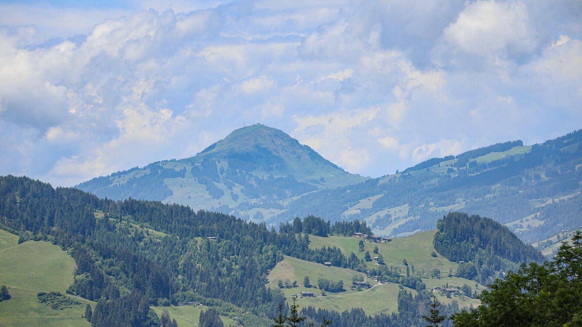 Sanfte grüne Hügel und bewaldete Berge in der Ferne unter einem hellen Himmel.