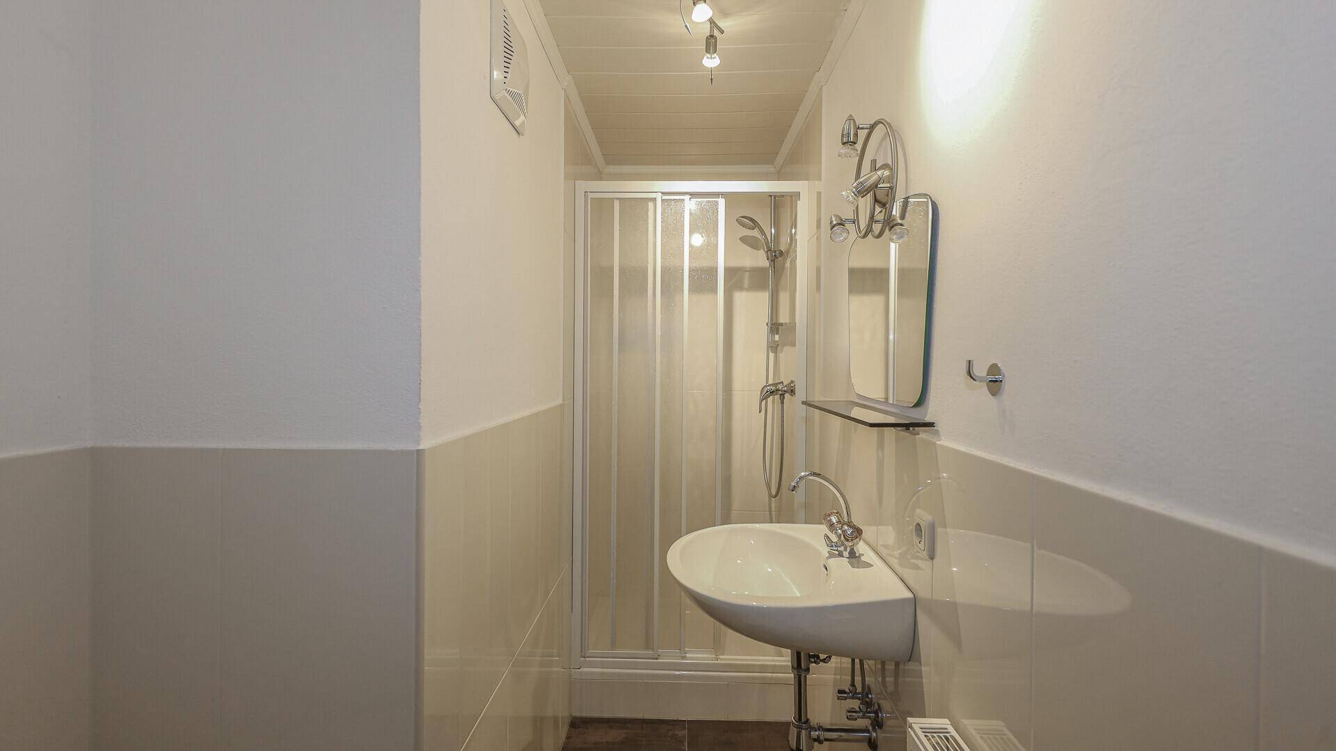 Kleines Badezimmer mit Duschkabine, Waschbecken und weißen Fliesen.