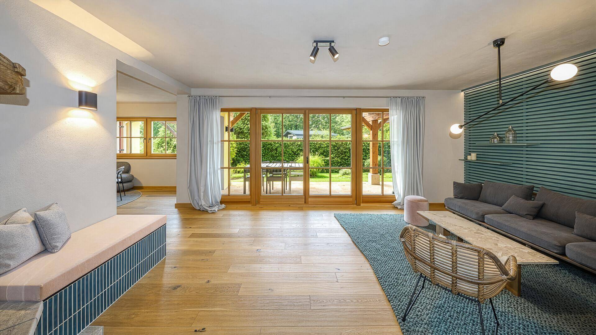 Geräumiges Wohnzimmer mit Holzboden und großen Fenstern, die den Blick ins Grüne freigeben.