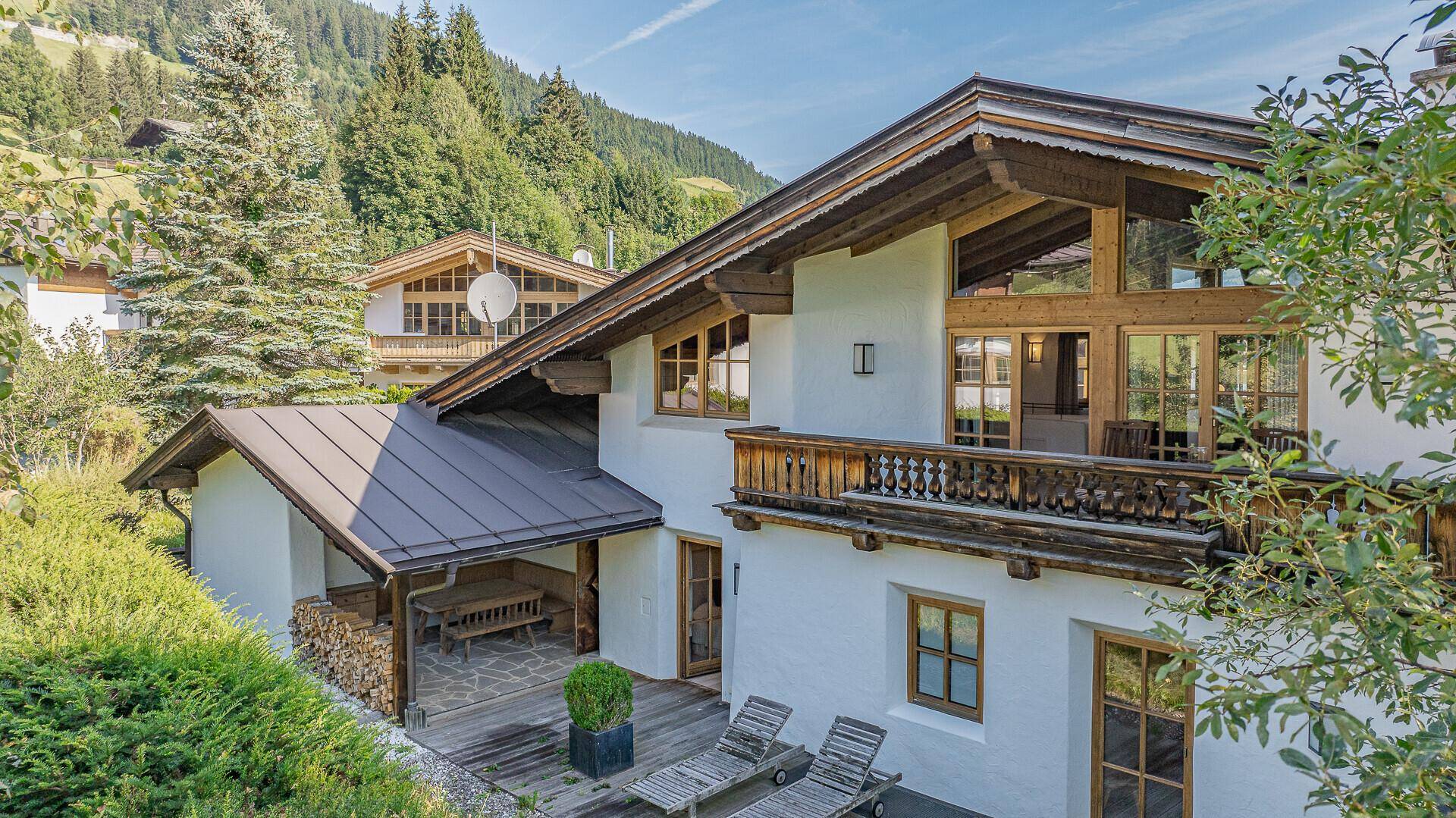 Seitenansicht des Hauses mit Holzterrasse, Balkon und grüner Umgebung.