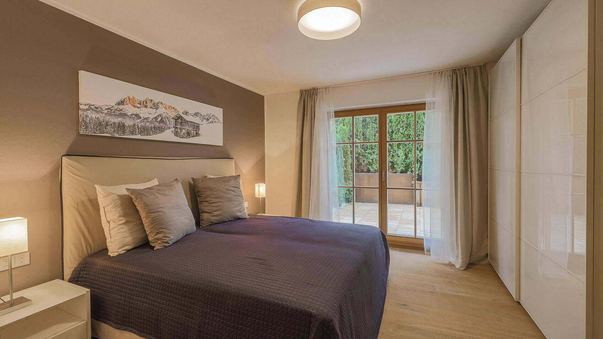 Helles Schlafzimmer mit großem Bett, Einbauschränken und Zugang zur Außenterrasse.
