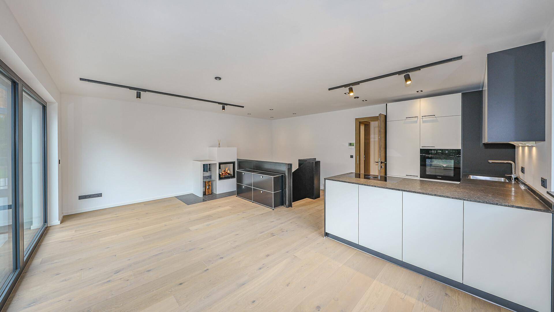 Heller offener Wohnbereich mit moderner Küche, Kamin und Holzboden.