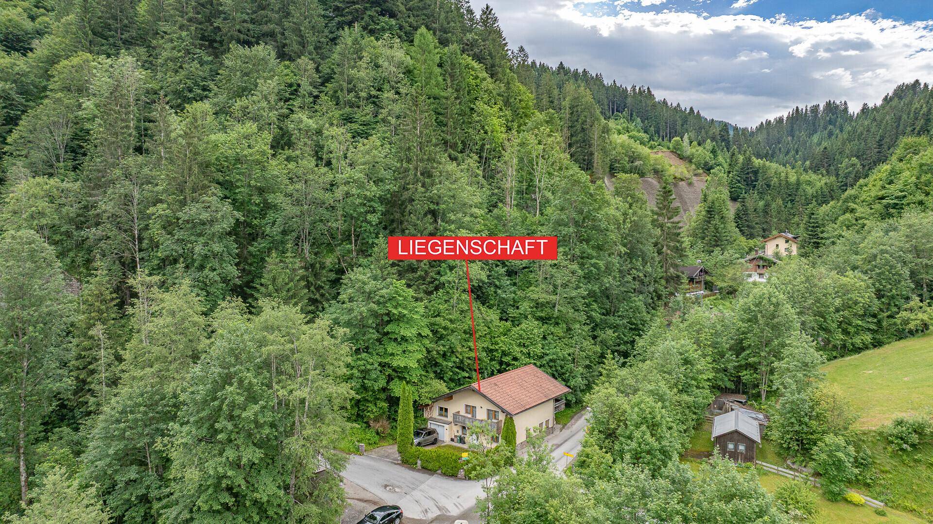 Weitläufige Luftaufnahme der Liegenschaft in einer bewaldeten Berglandschaft.