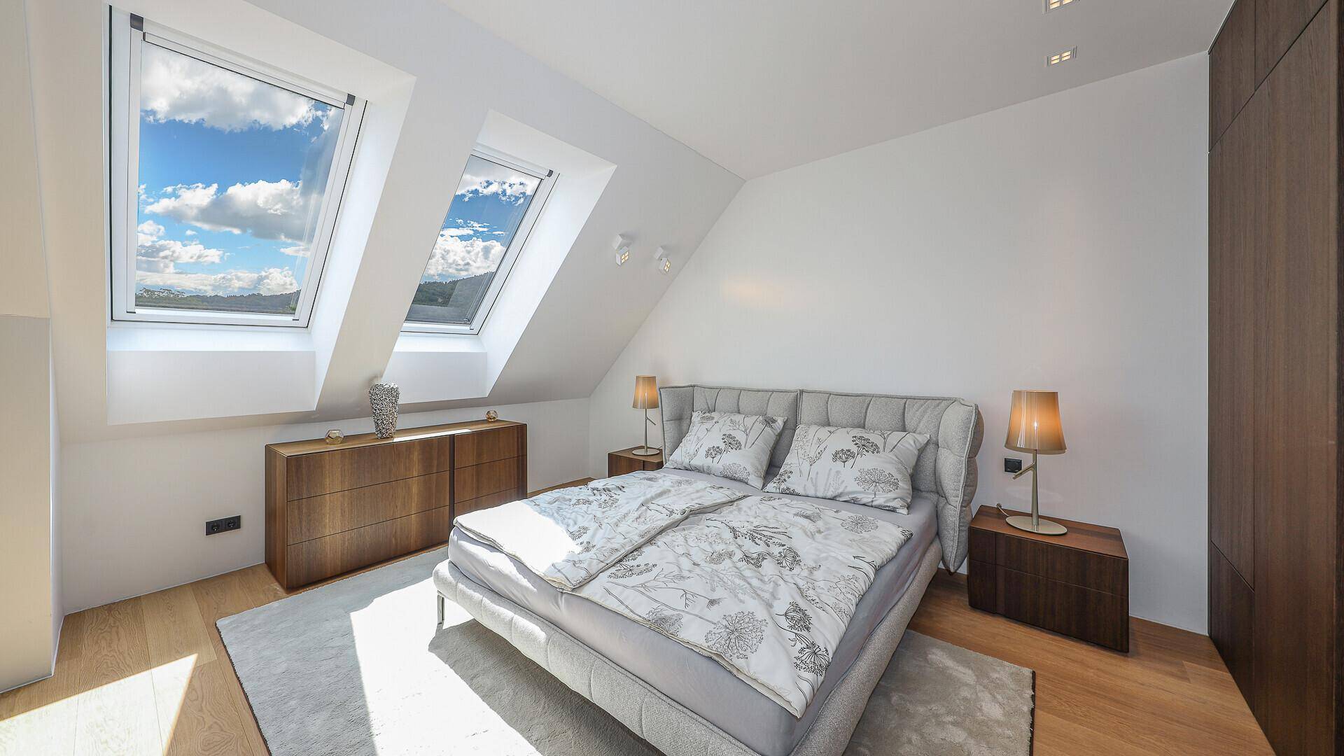Helles Schlafzimmer im Dachgeschoss mit zwei Dachfenstern und Holzboden.