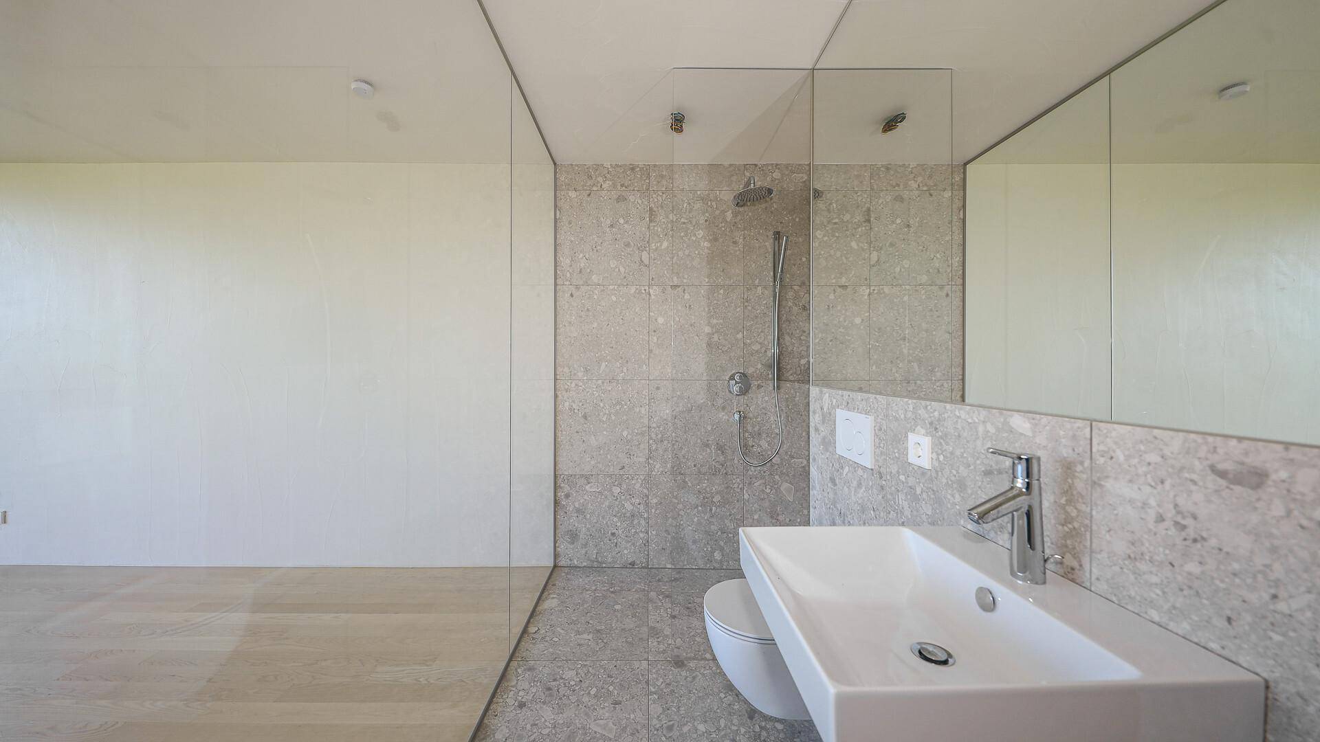 Helles Badezimmer mit modernen Fliesen, begehbarer Dusche und großem Spiegel.