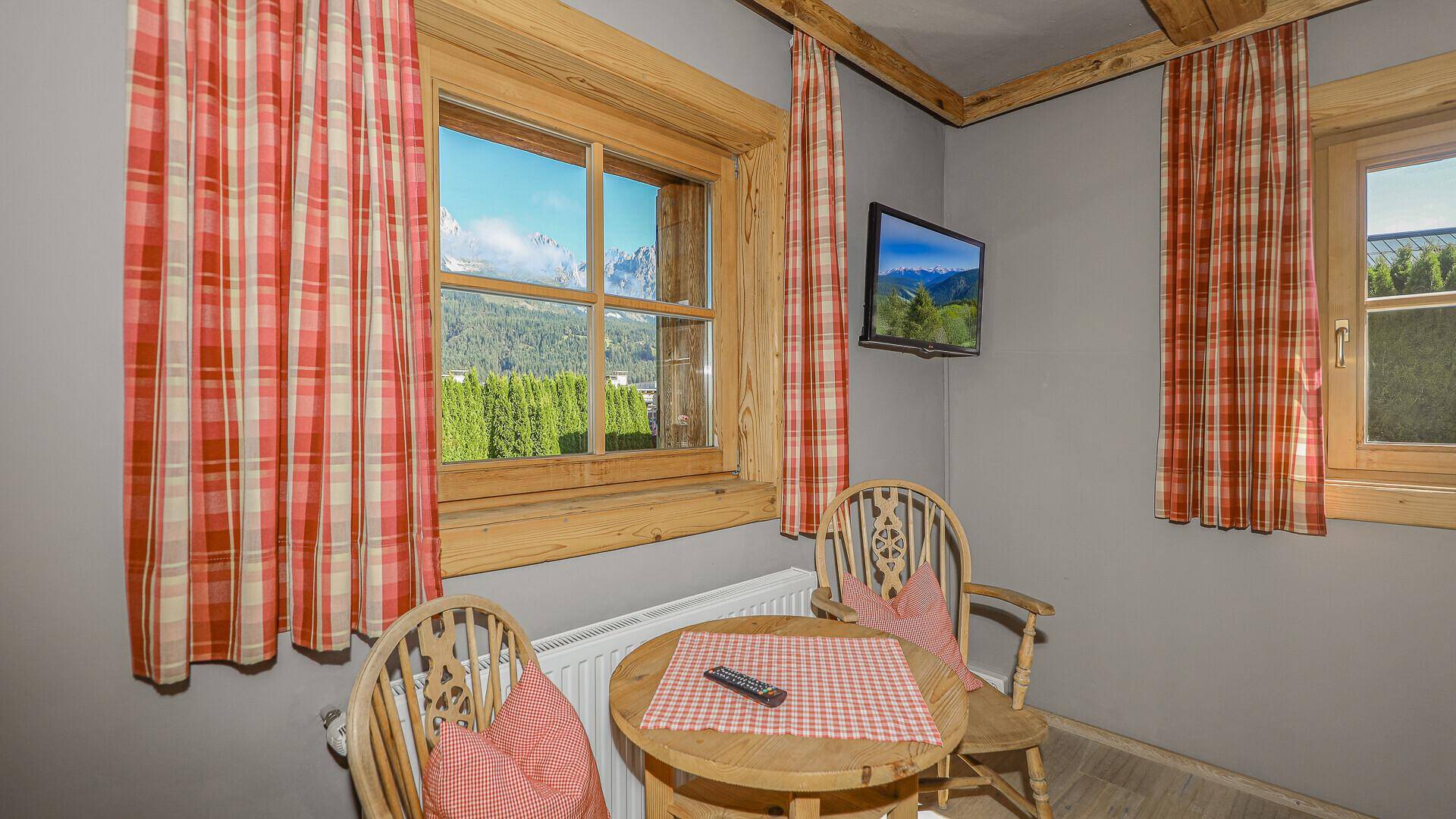 Schlafzimmer mit Sitzgelegenheit, Bergblick und traditionellen karierten Vorhängen.